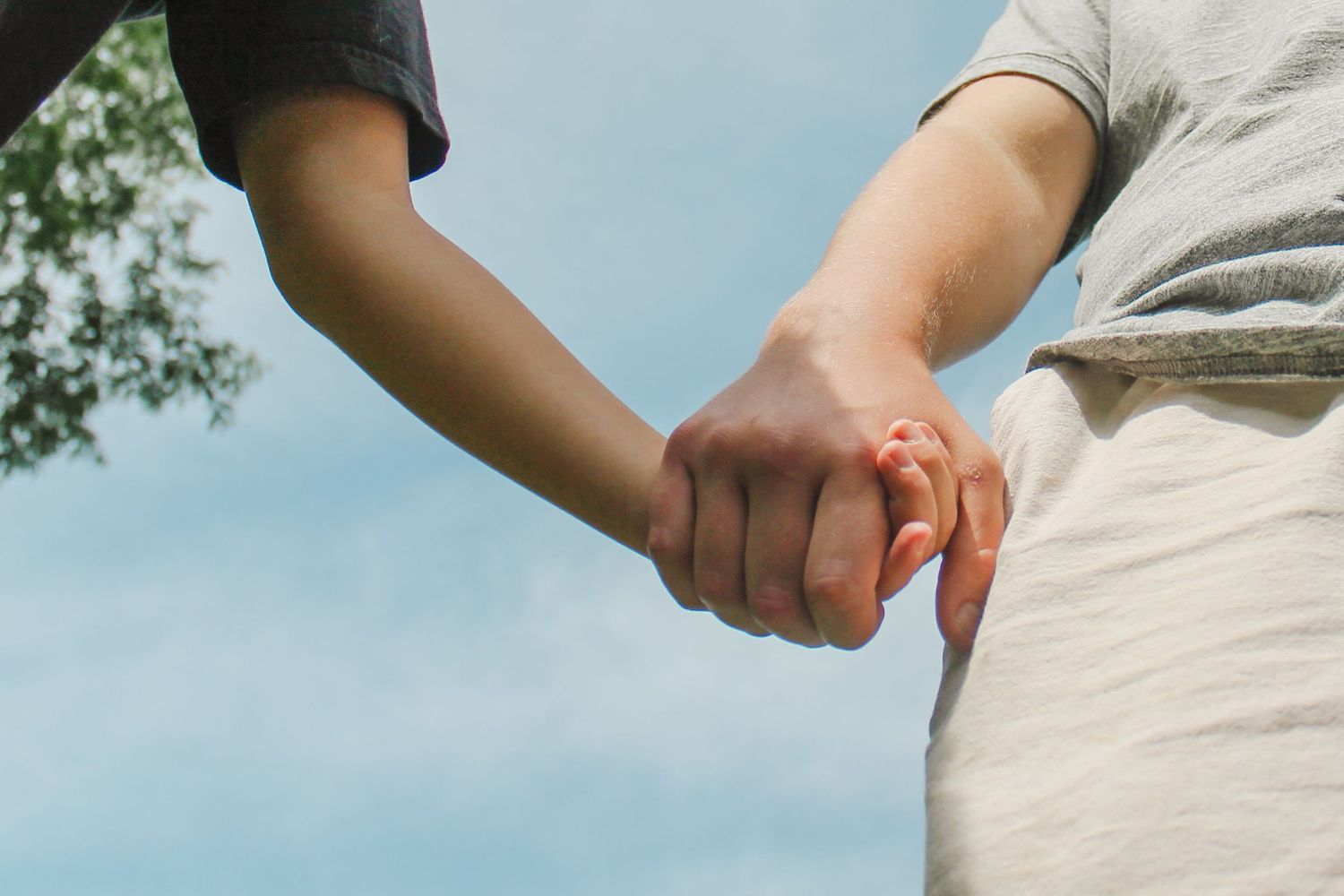 Two people hold hands together against a bright blue sky background.
