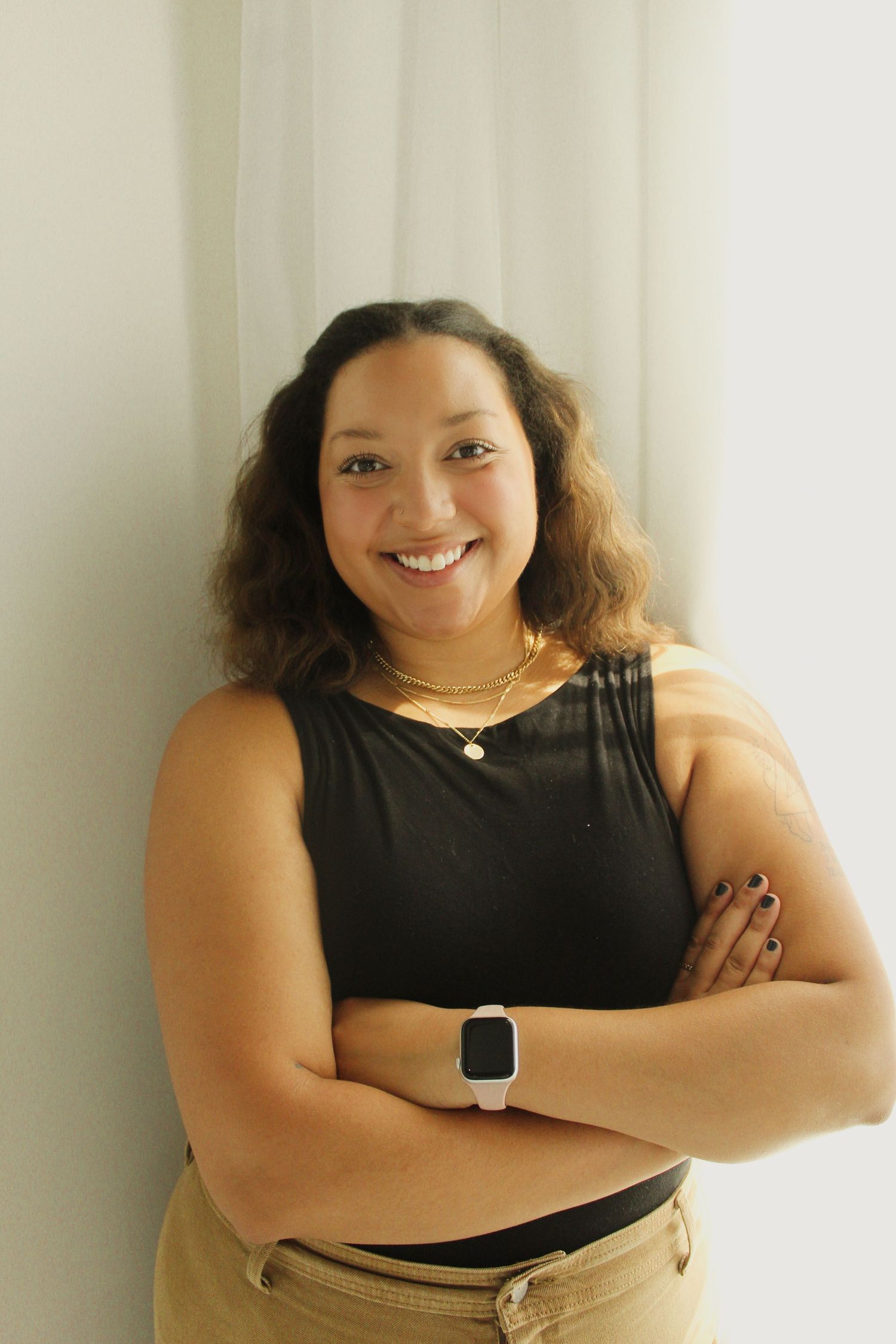 Woman in black sleeveless top with smartwatch poses confidently against white background.