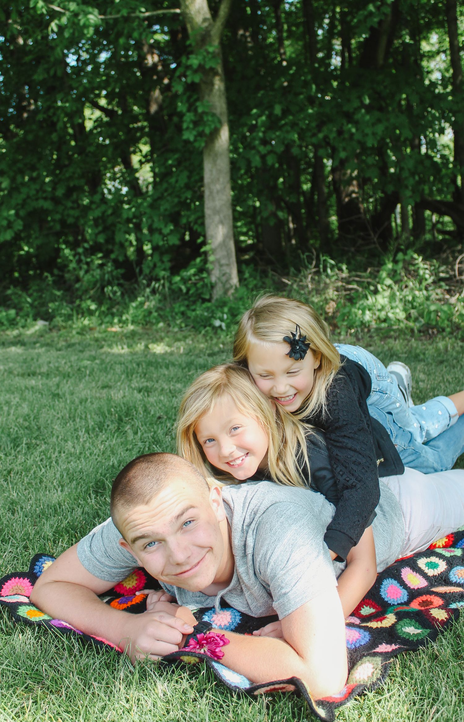 Family enjoys a relaxed moment together while laying on a colorful blanket in a lush green forest setting.