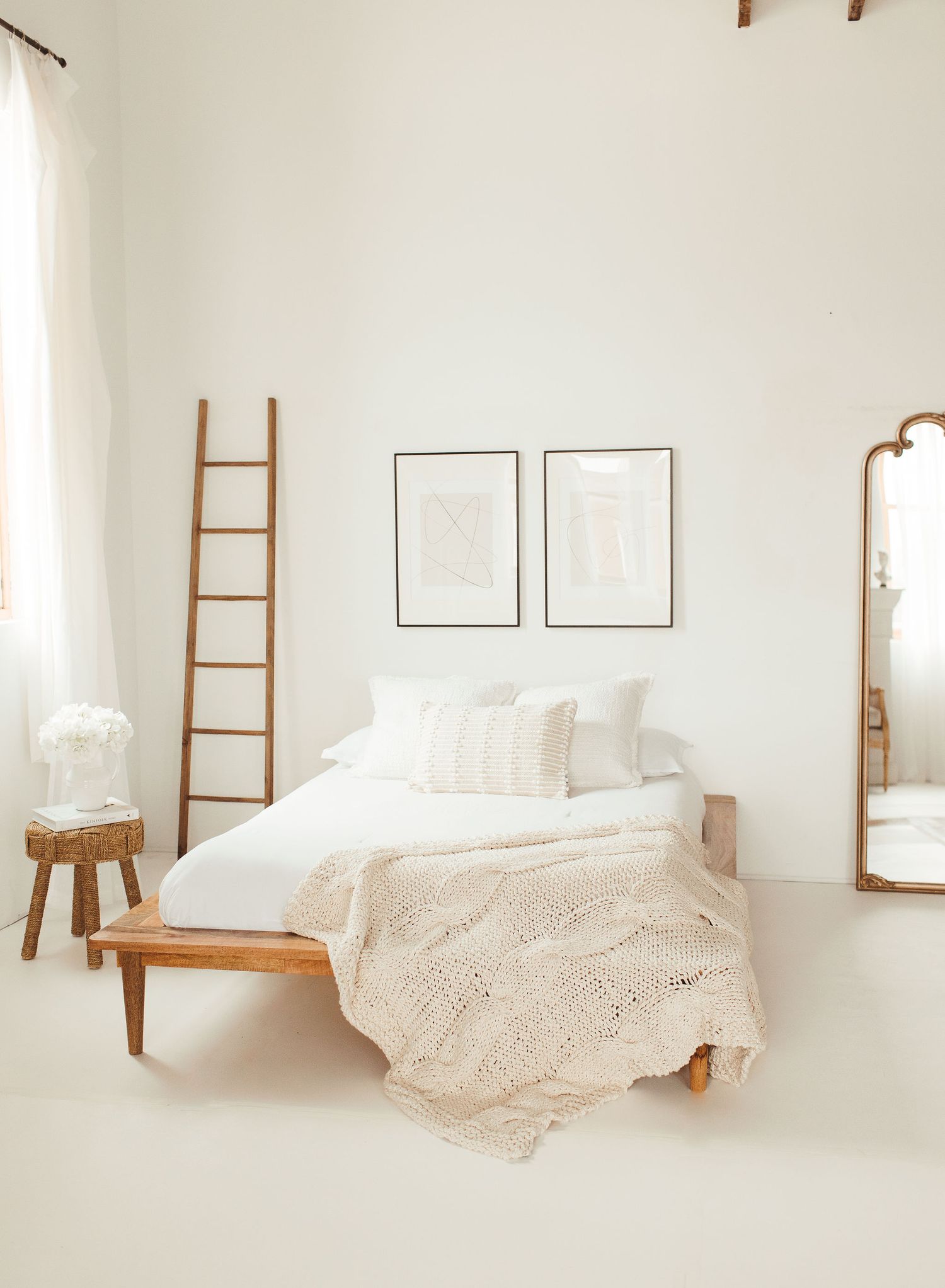 Minimalist white bedroom interior with wooden ladder and soft textiles.