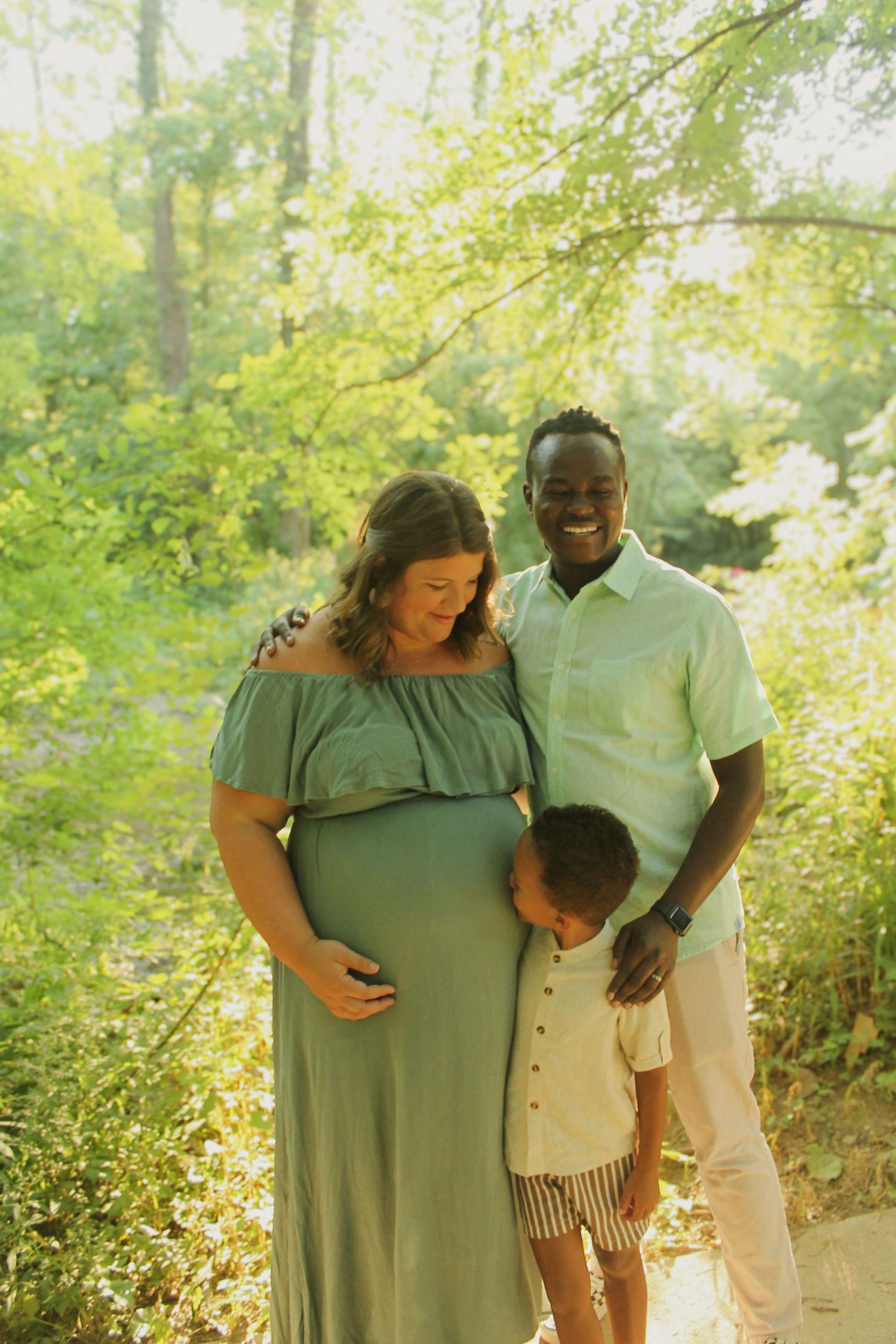 Family photo session in a sunlit forest setting with soft green foliage.