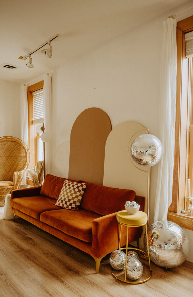 Modern living room corner with brown velvet sofa, golden side table, and decorative glass orbs in a warm-toned setting.