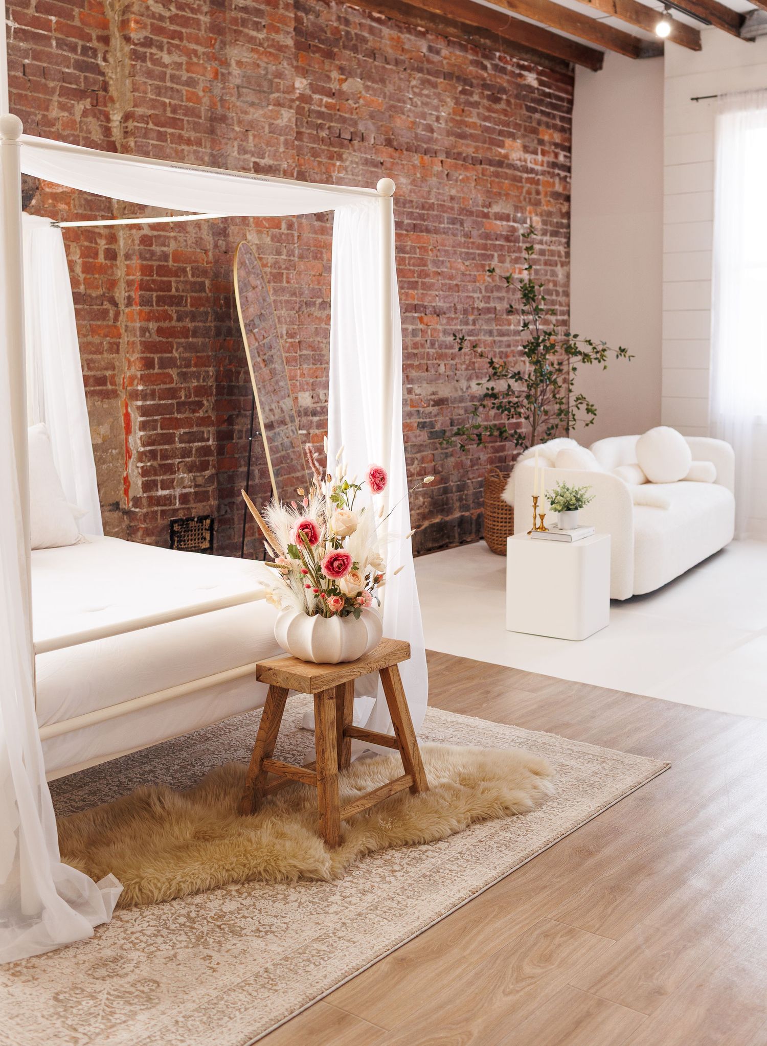 Studio space with exposed brick wall, white curtains, and hardwood flooring.