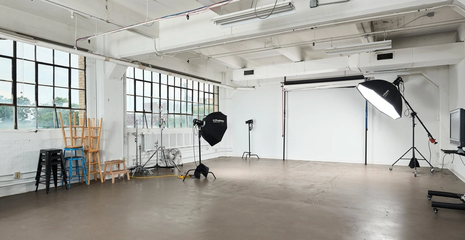A wide angle view of an empty industrial warehouse space with large windows and exposed ceiling beams.