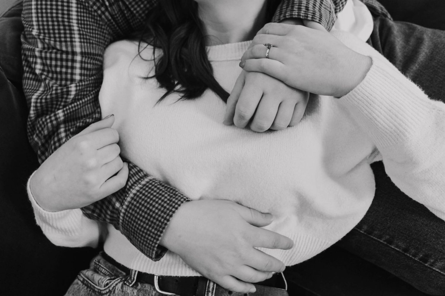 Black and white close-up of couple's hands embracing in intimate moment.