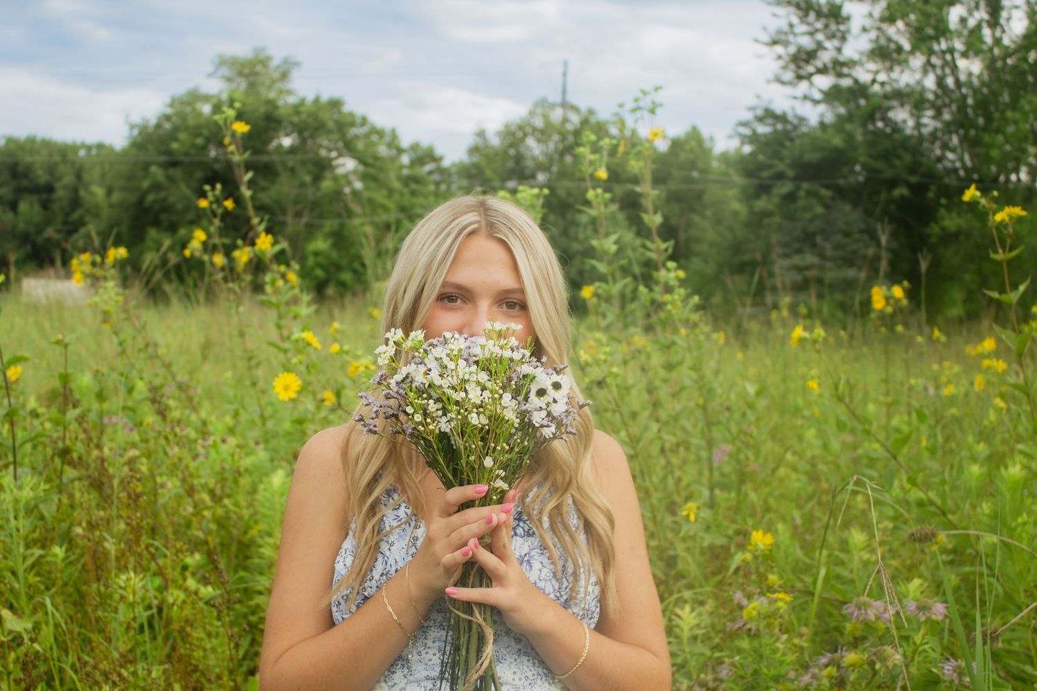 Person lying in wildflower meadow with yellow flowers and blue sky.