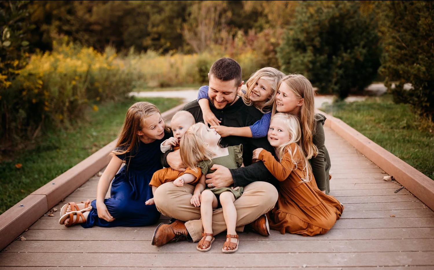 A joyful family shares a tender moment together while sitting on a wooden boardwalk in nature.