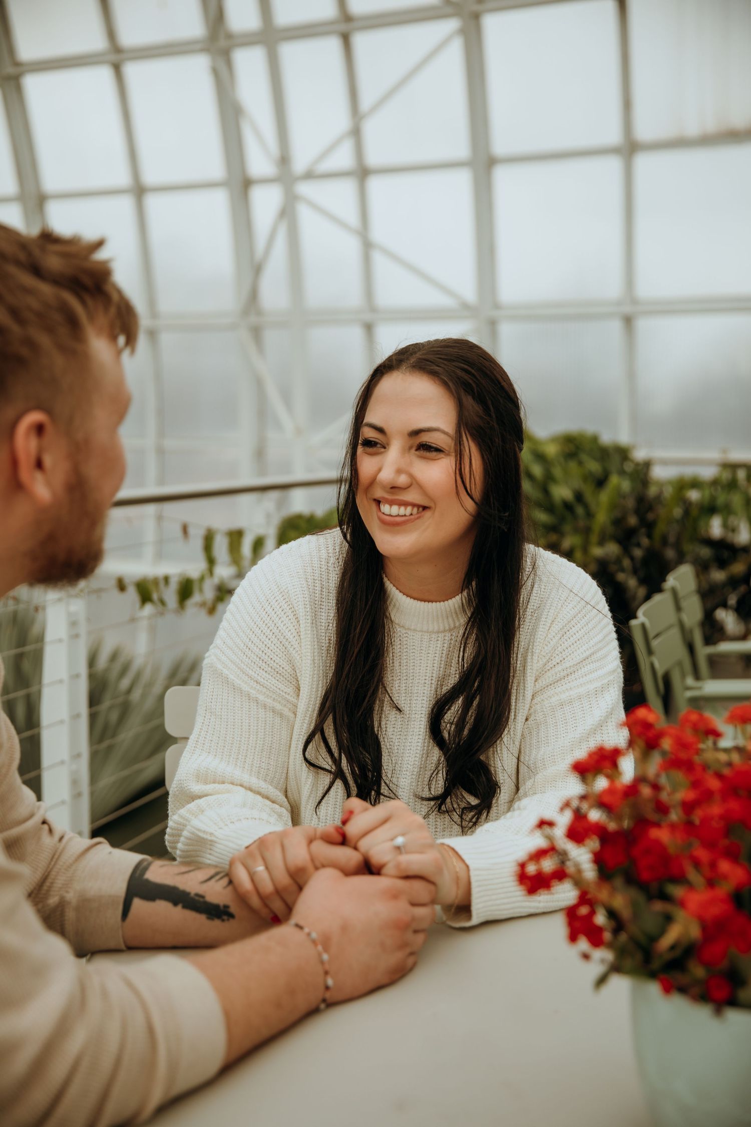 Couple shares intimate moment in greenhouse with red flowers.