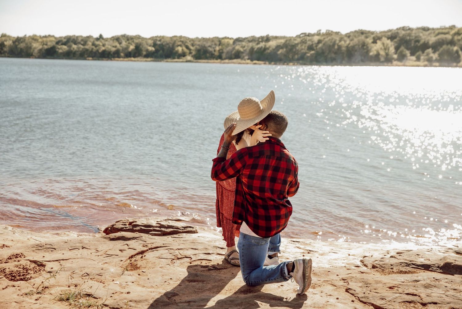 A couple sharing a tender moment by the lake while wearing casual outdoor attire.