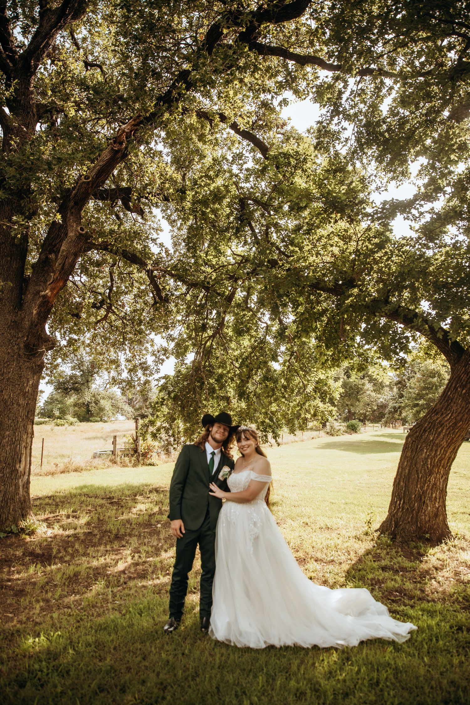 Wedding couple poses under majestic oak trees in golden afternoon light.