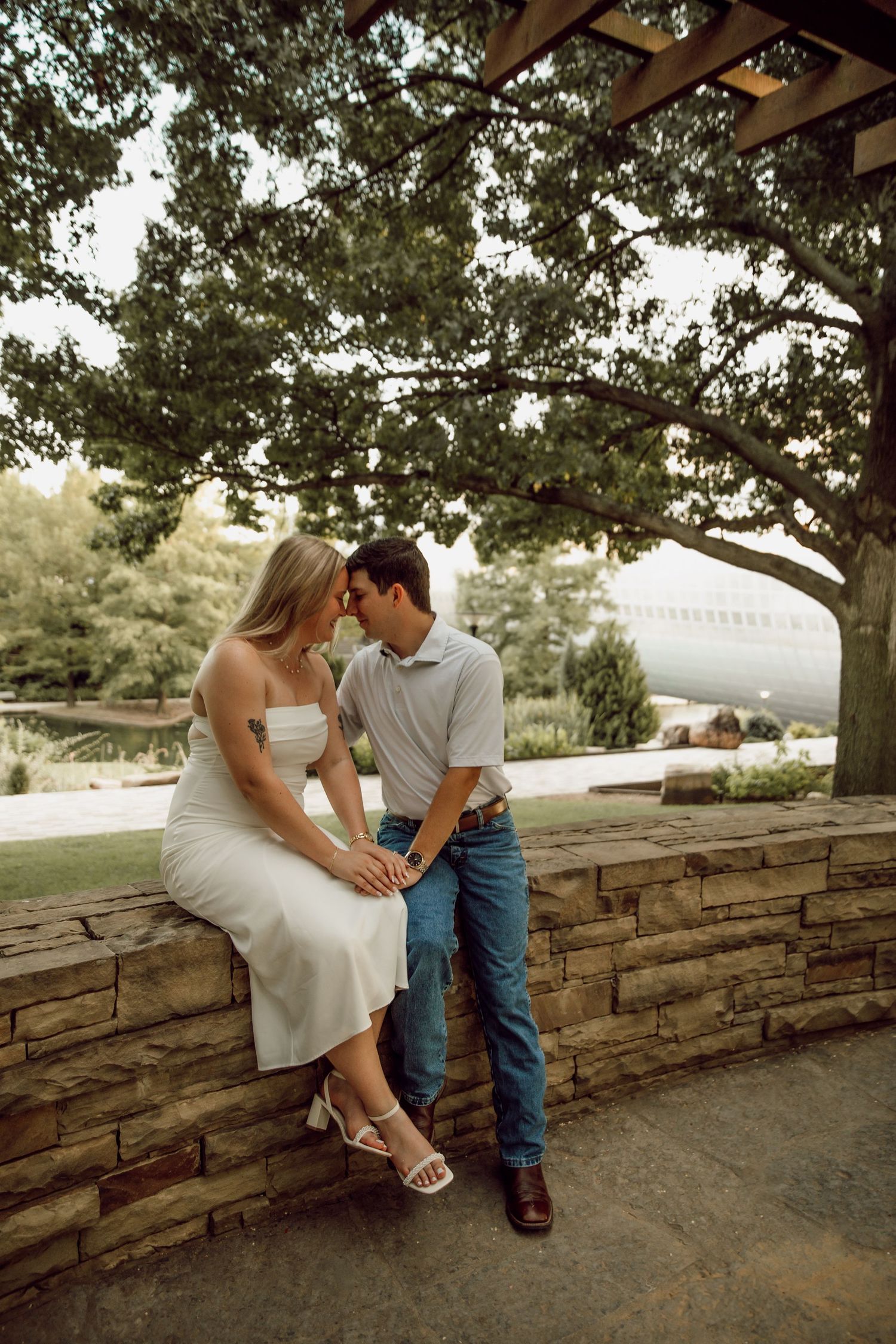 Romantic couple shares tender moments while sitting on stone wall in outdoor setting.