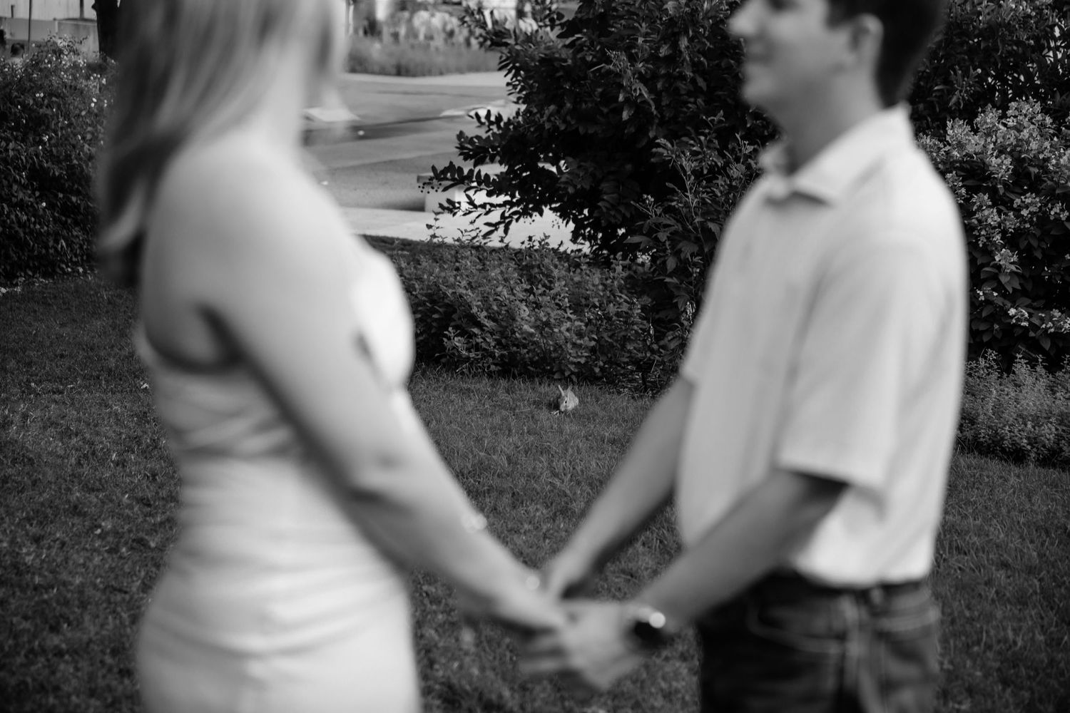 An intimate black and white photo of a couple holding hands in a garden.