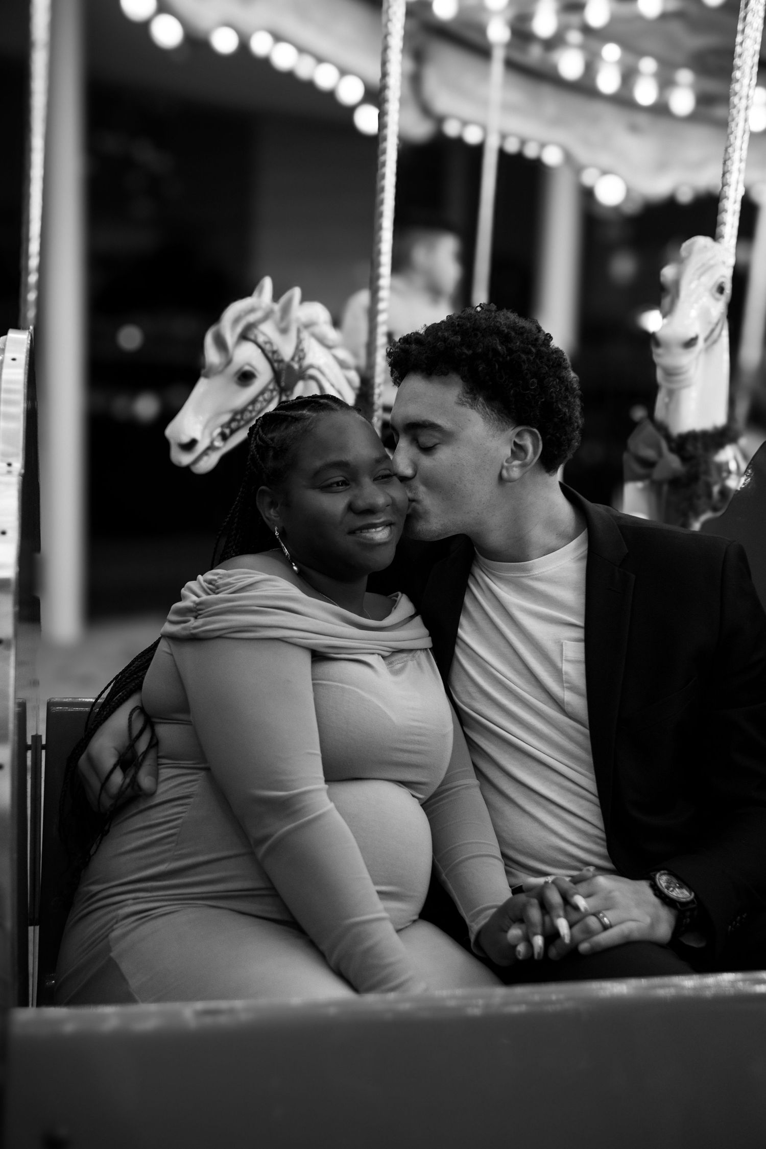 Black and white photo of a couple sharing tender moments while riding a carousel.
