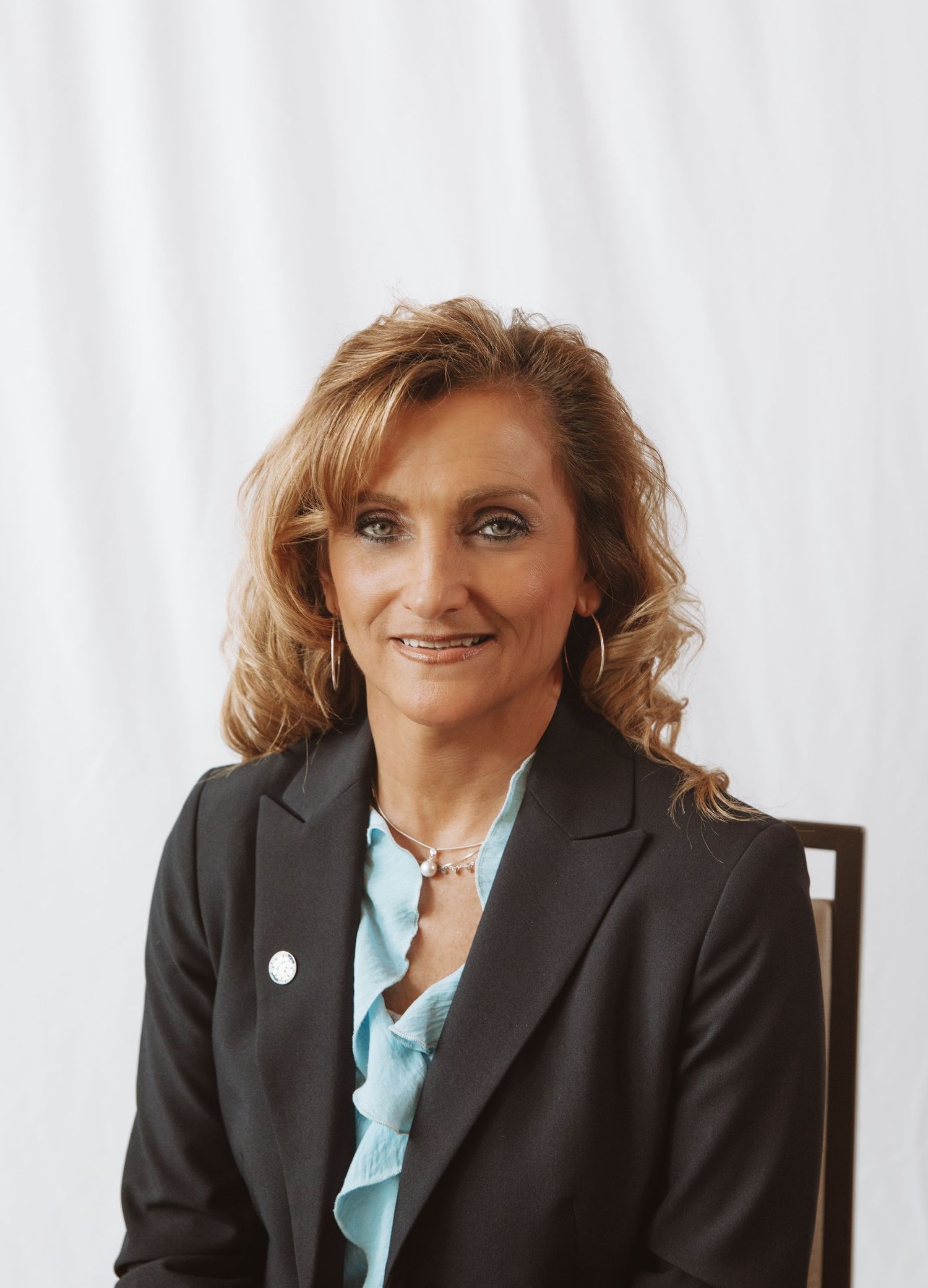 Professional headshot of someone in a dark business suit and light blue blouse smiling warmly at the camera.