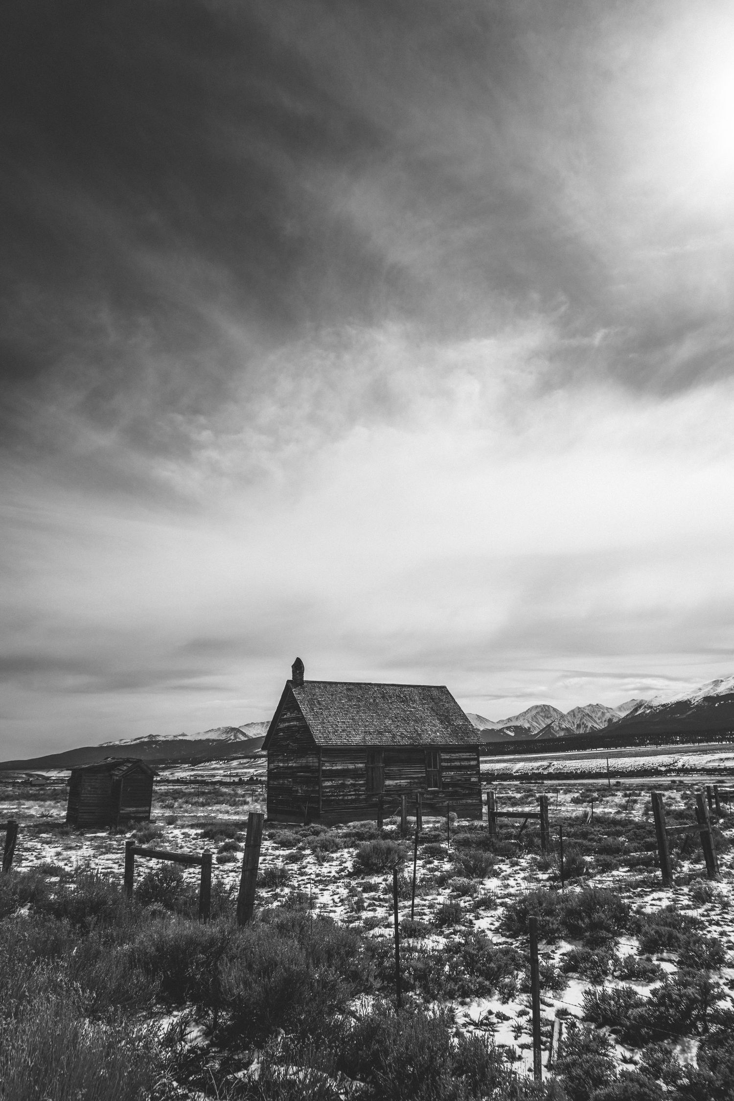 Dramatic black and white panoramic landscape with mountains and old buildings under cloudy skies.