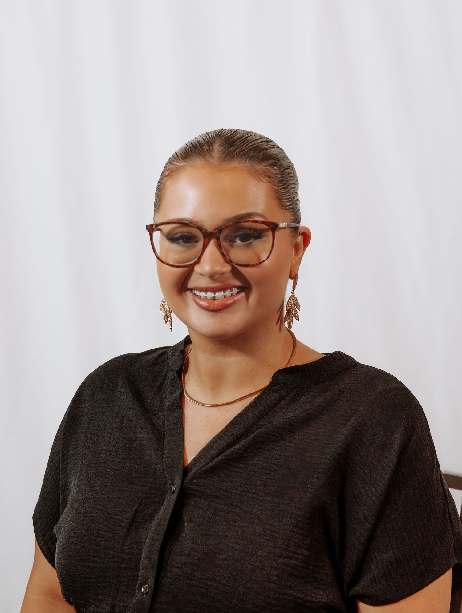 Professional headshots of someone wearing black attire and stylish cat-eye glasses against a white background.