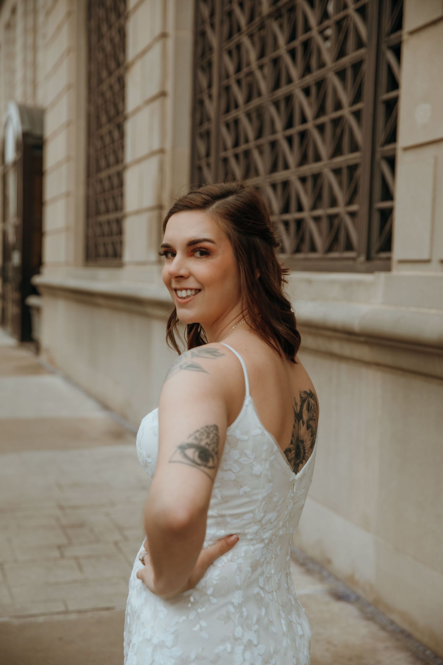 Bride in lace wedding dress poses against stone architectural details.