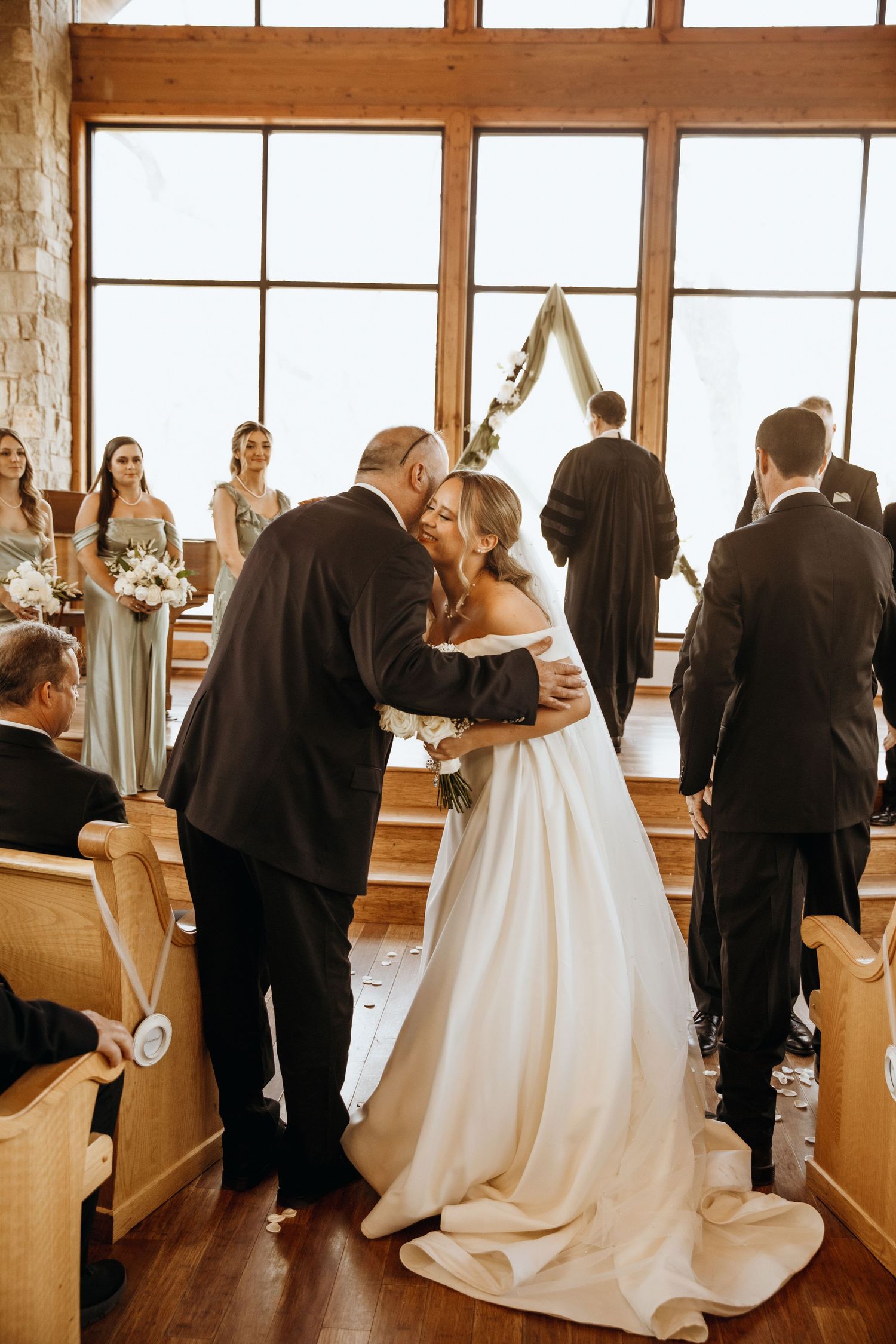 Panoramic view of a wedding ceremony in a rustic chapel with wooden beams and large windows.
