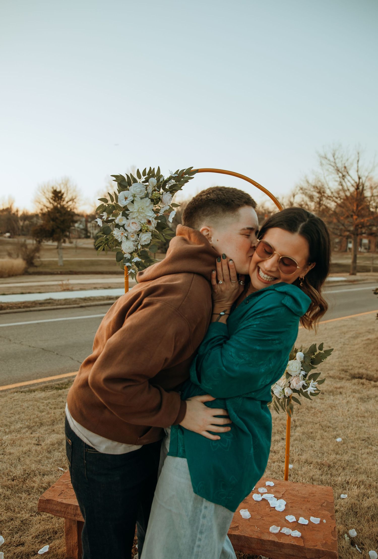 A romantic couple shares a tender moment by a decorated arch in an outdoor setting.