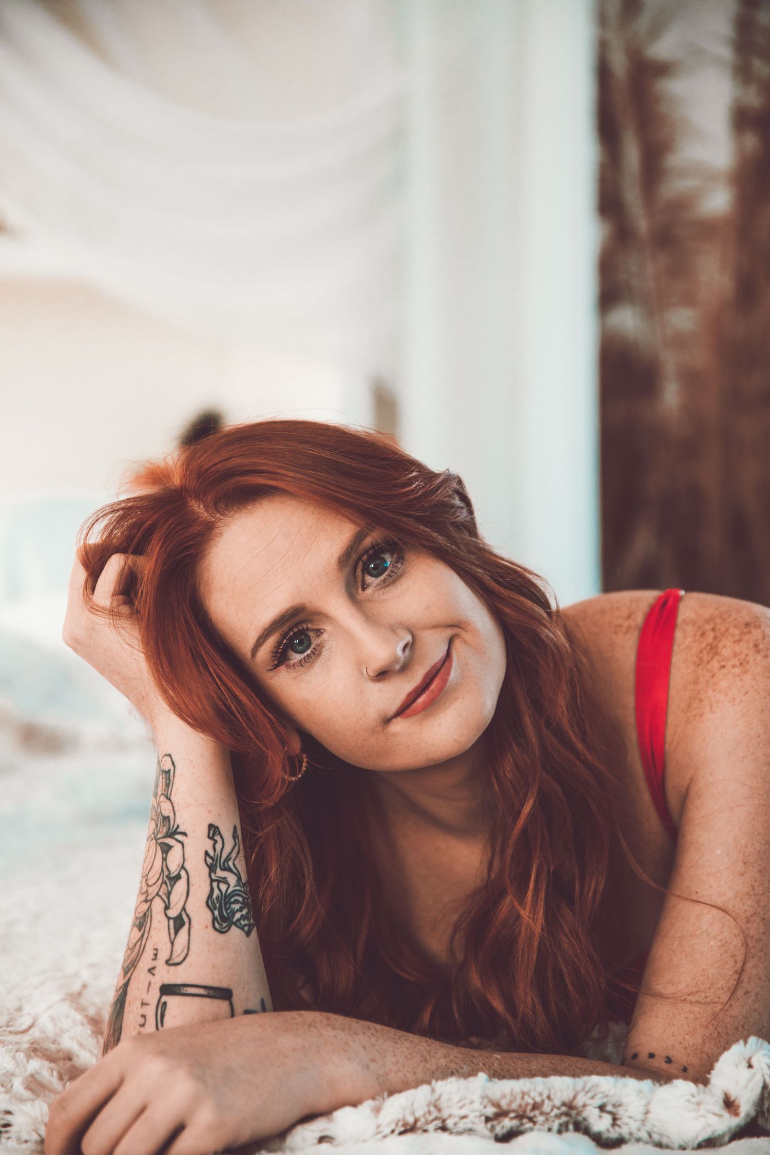 Person with red hair poses on white textured surface in intimate boudoir photoshoot.