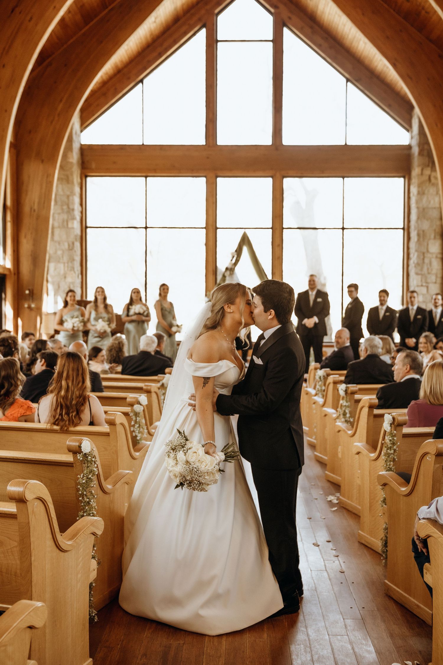 Church wedding ceremony with wooden interior and natural light streaming through windows.