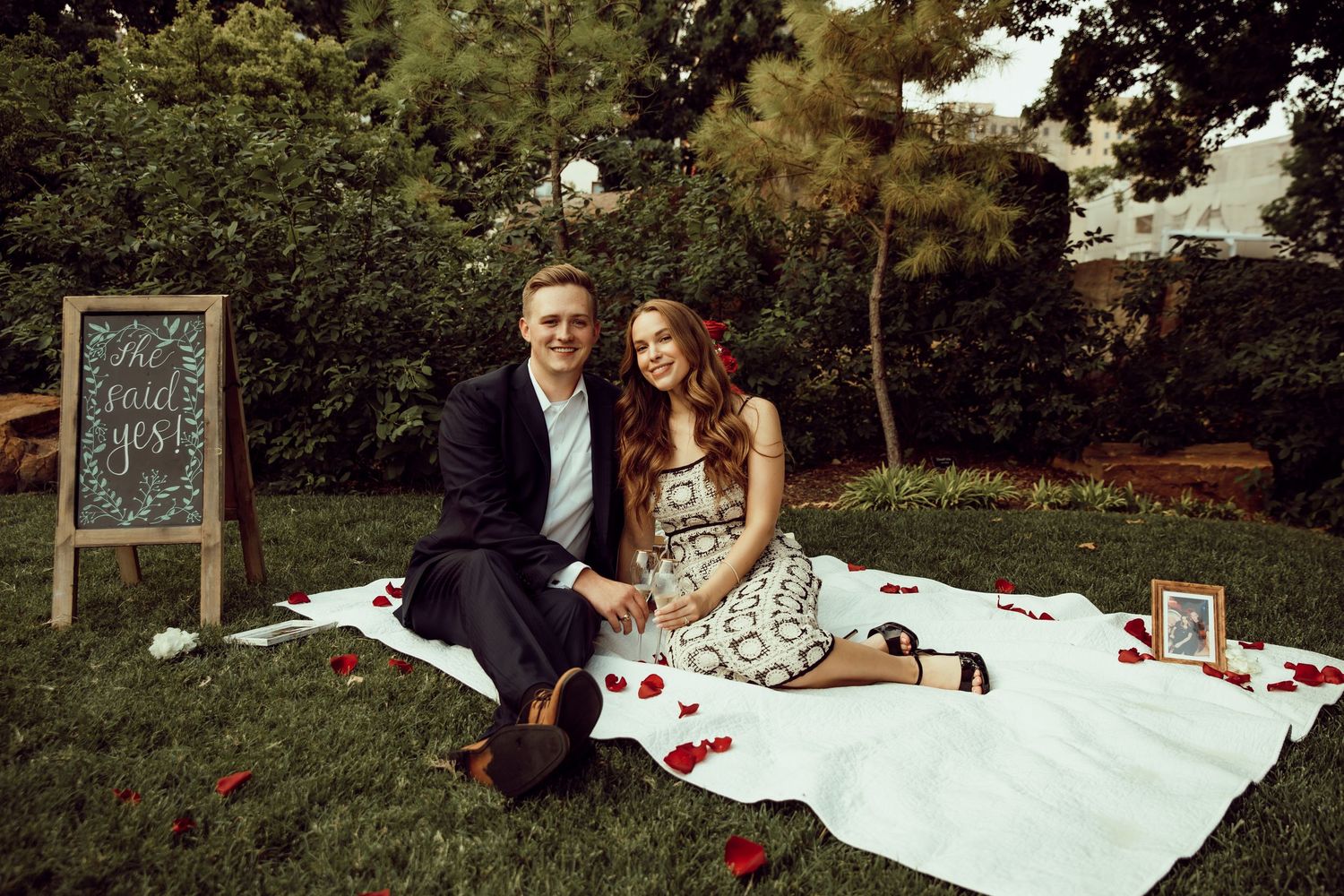 A couple enjoying a romantic picnic on a blanket with a chalkboard sign nearby.