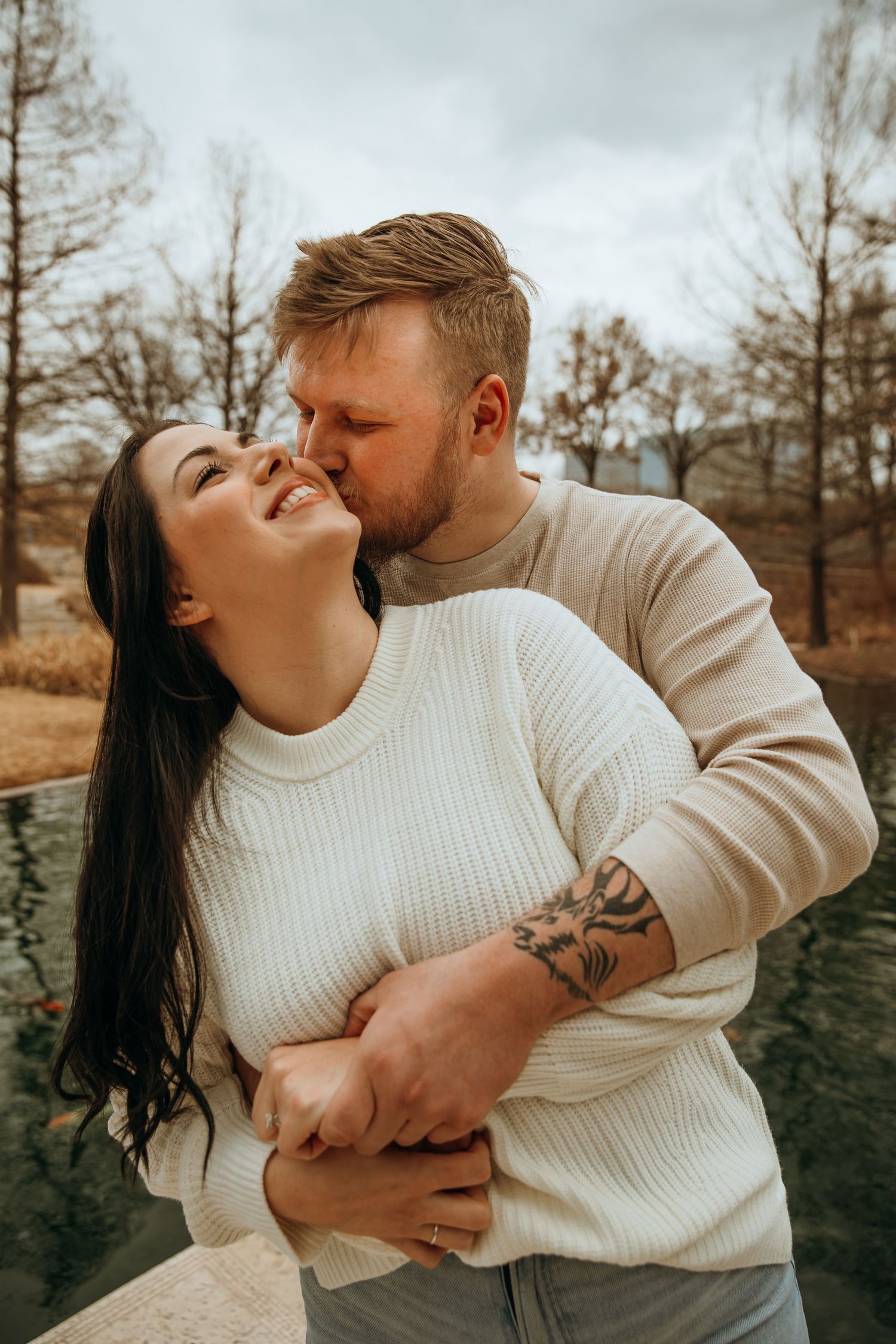 Couple in matching white sweaters embraces during winter photo session.