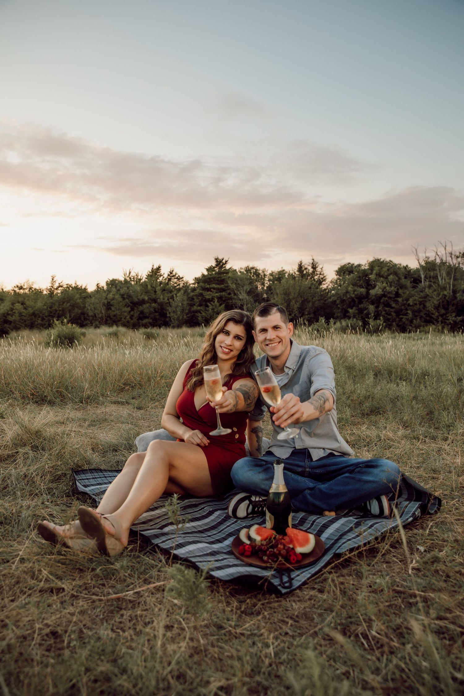 A couple enjoys a picnic on a blanket in a grassy field at sunset.