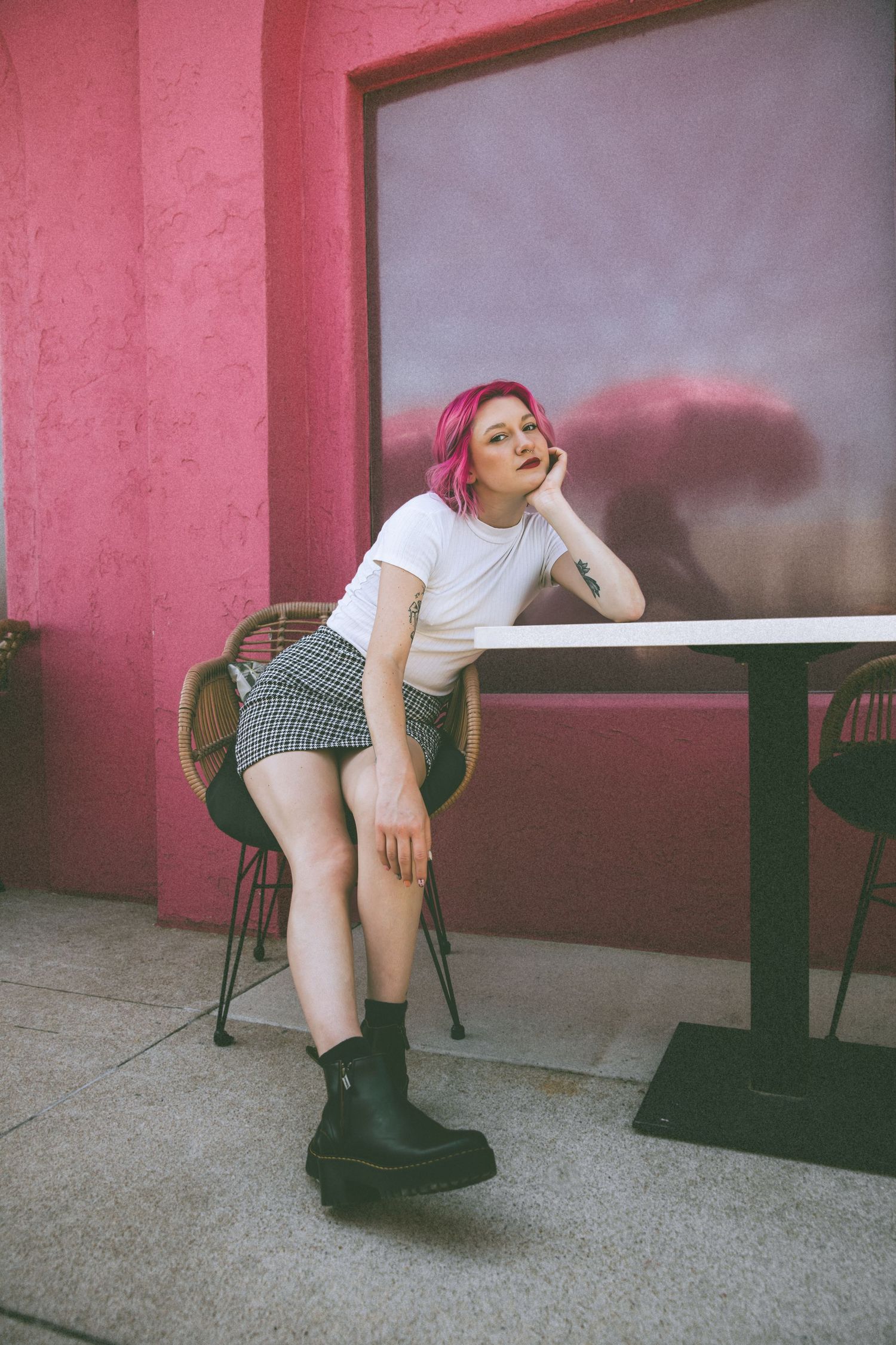 Artistic portrait of someone wearing boots while sitting against pink wall background.