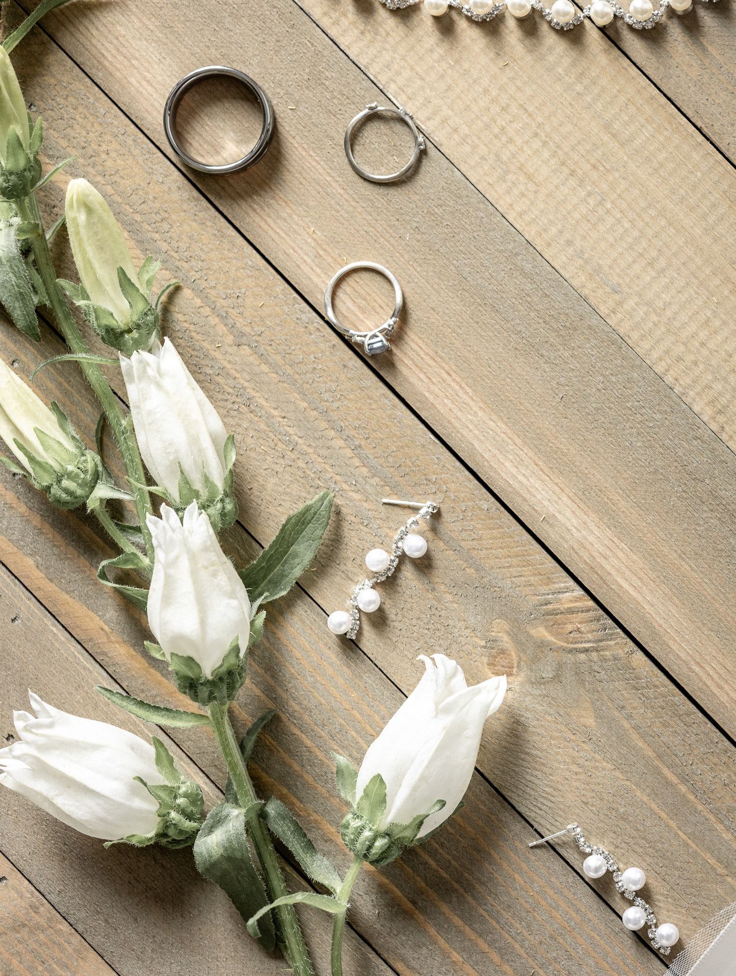 Bozeman Wedding detail of rings and pearl earrings displayed with white flowers on rustic wooden boards. Photo by Kelsea Laine Photography.