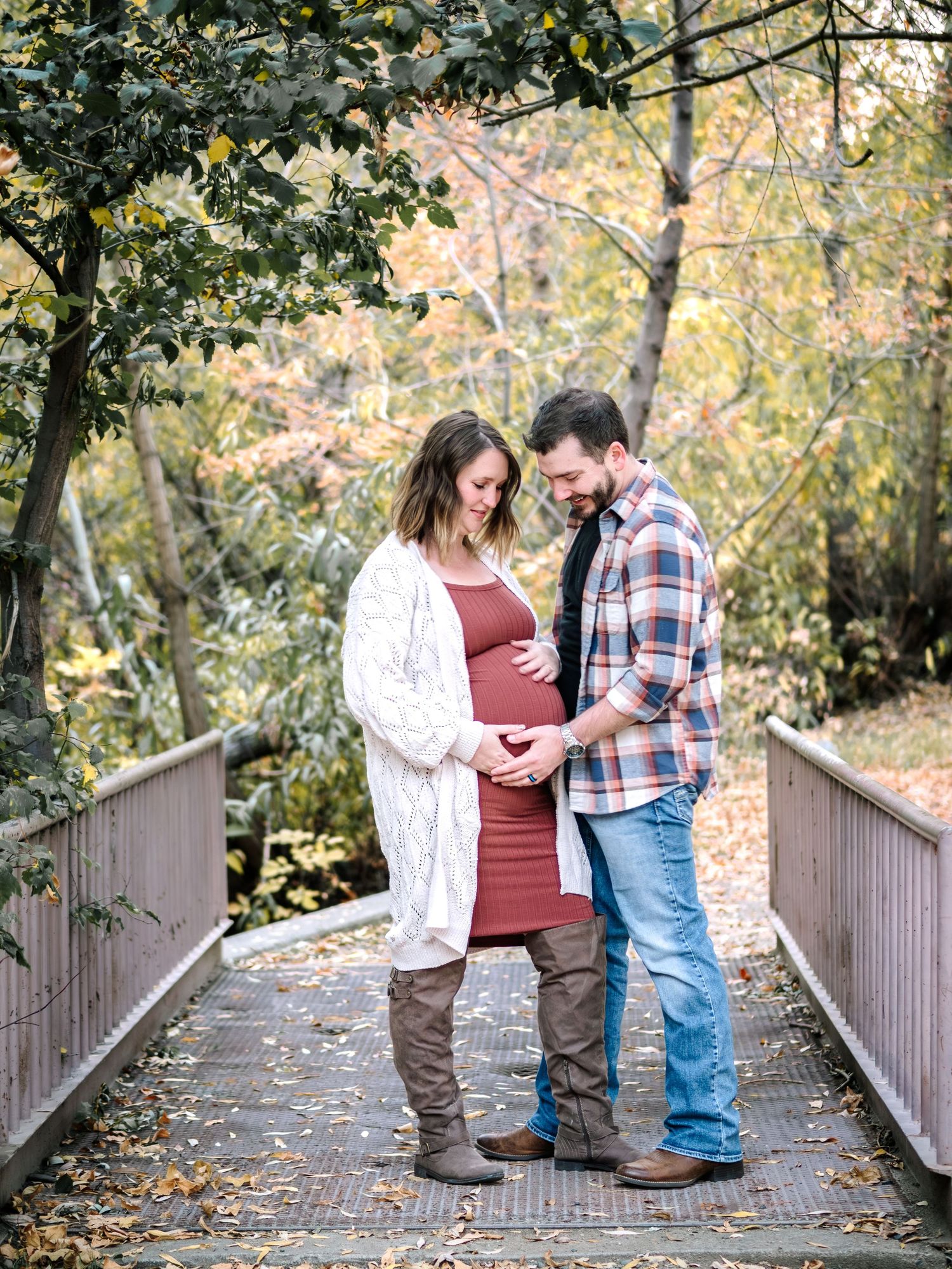 Couple embraces on rustic bridge path during fall maternity photoshoot. A maternity photo by Helena photographer Kelsea Laine Photography.