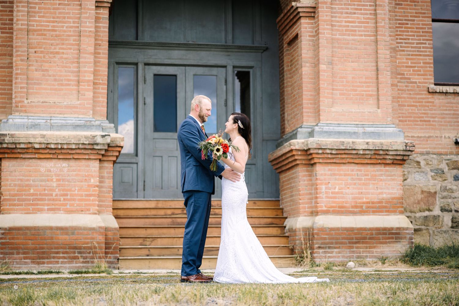 A bride and groom share a romantic moment outside a historic brick church with grand columns.