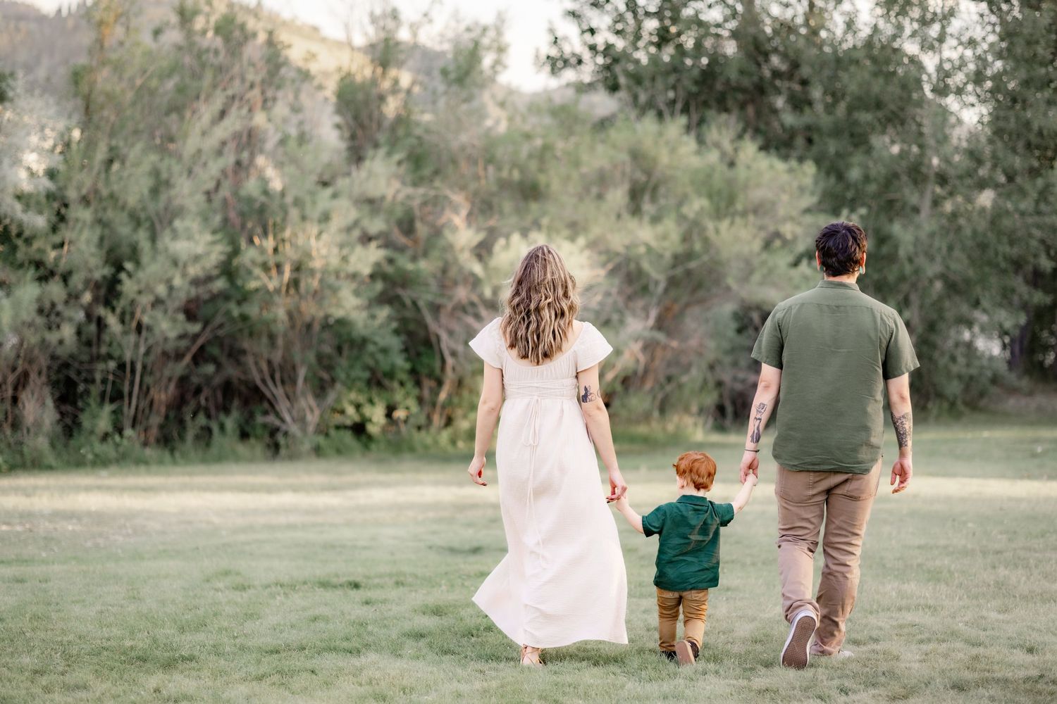 Family walks hand in hand through grassy field at sunset. A family portrait by Helena photographer Kelsea Laine Photography.