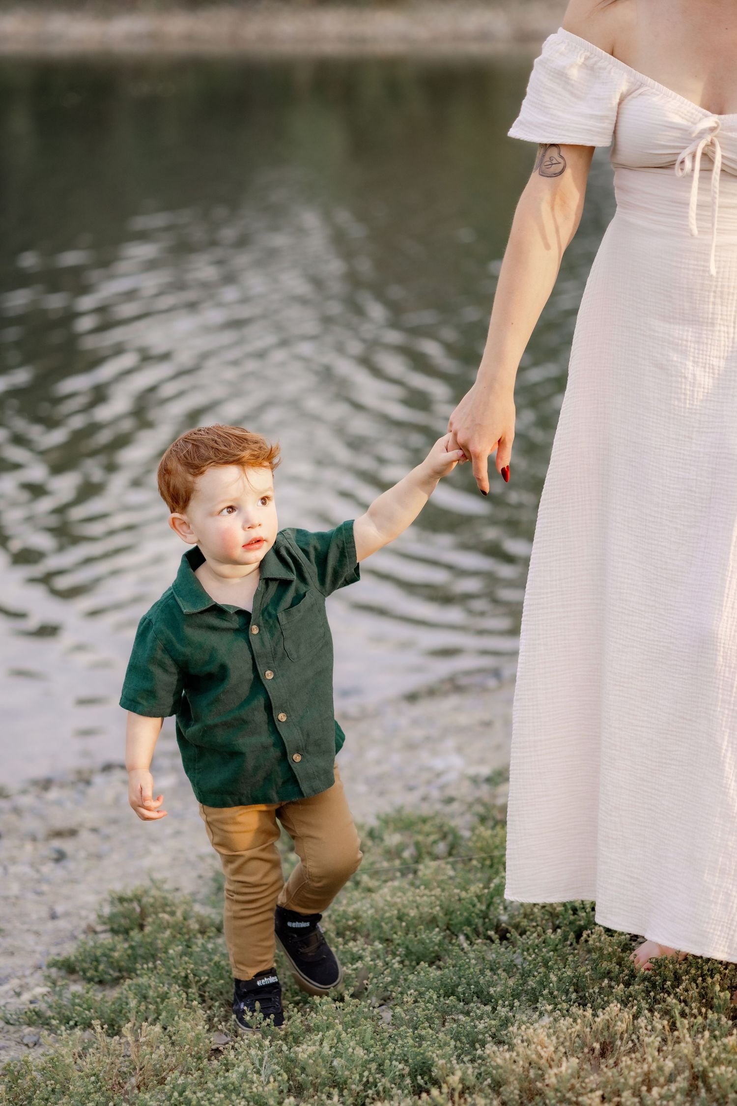 Child in green shirt and khaki pants plays by the water's edge. A photo by Montana photographer, Kelsea Laine Photography.