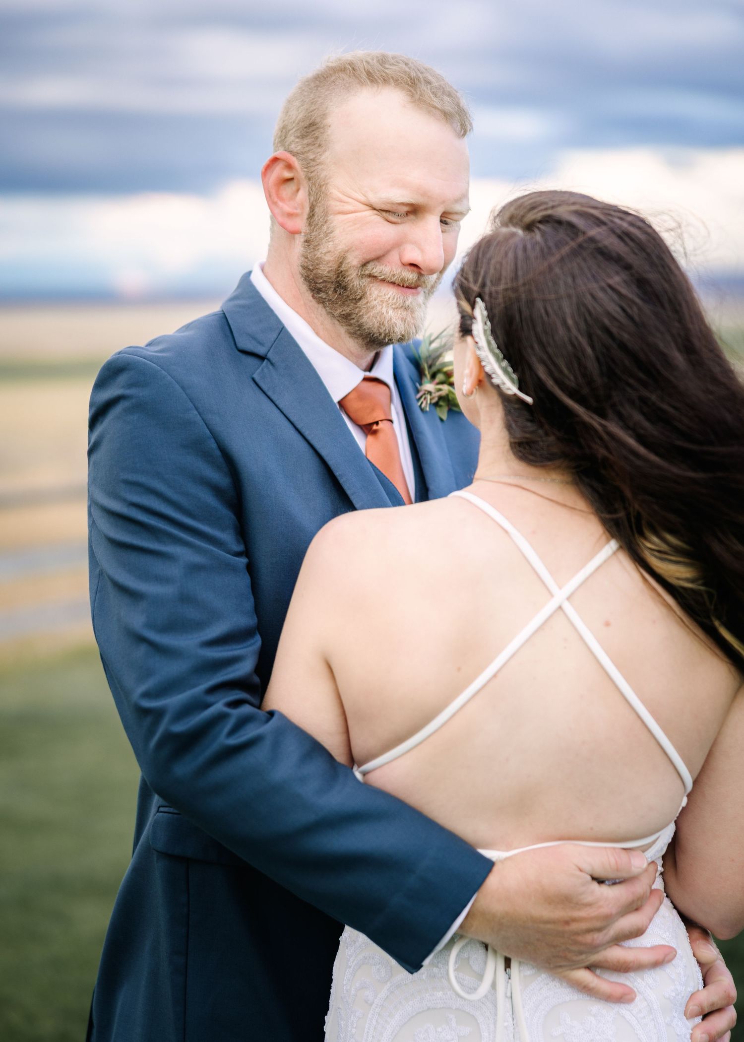 A tender moment between newlyweds embracing outdoors with scenic landscape and cloudy sky in the background.