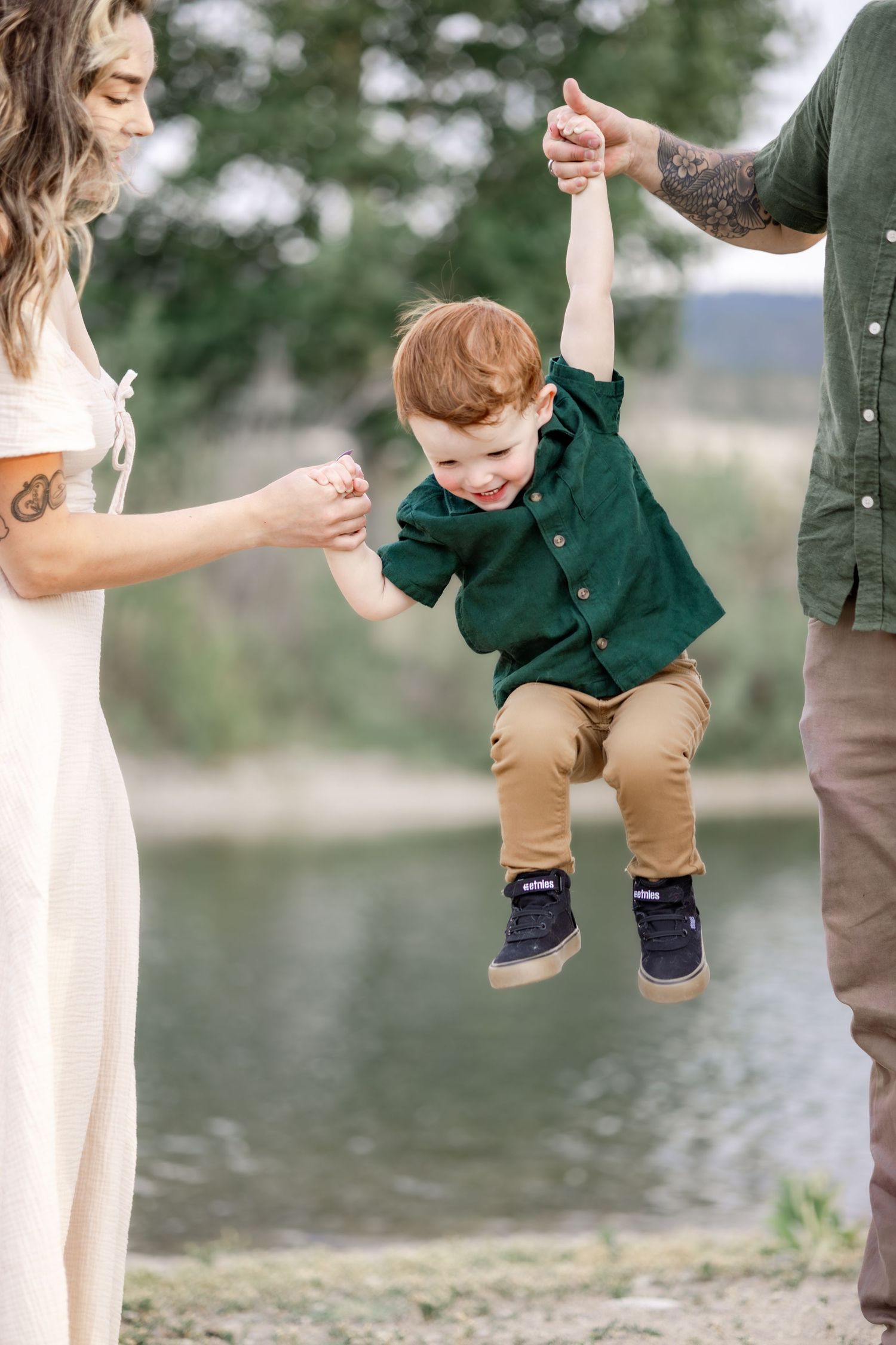 A playful moment swinging a small child in a green shirt between two adults. A family portrait by Kelsea Laine Photography.