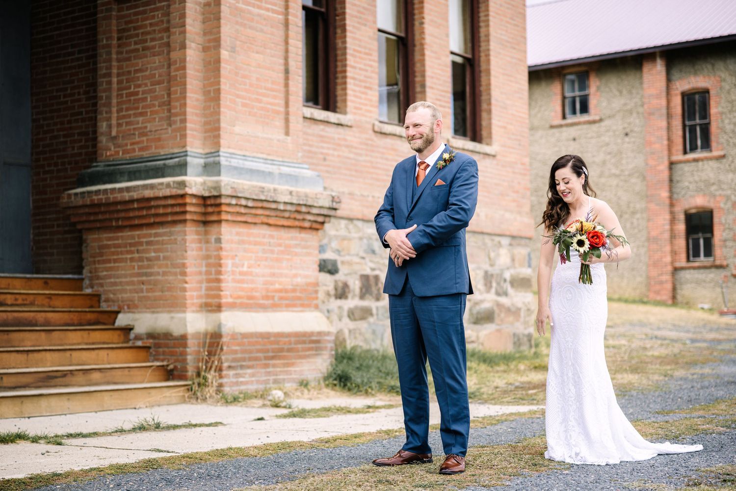 A couple in wedding attire poses together on stone steps outside a brick building.