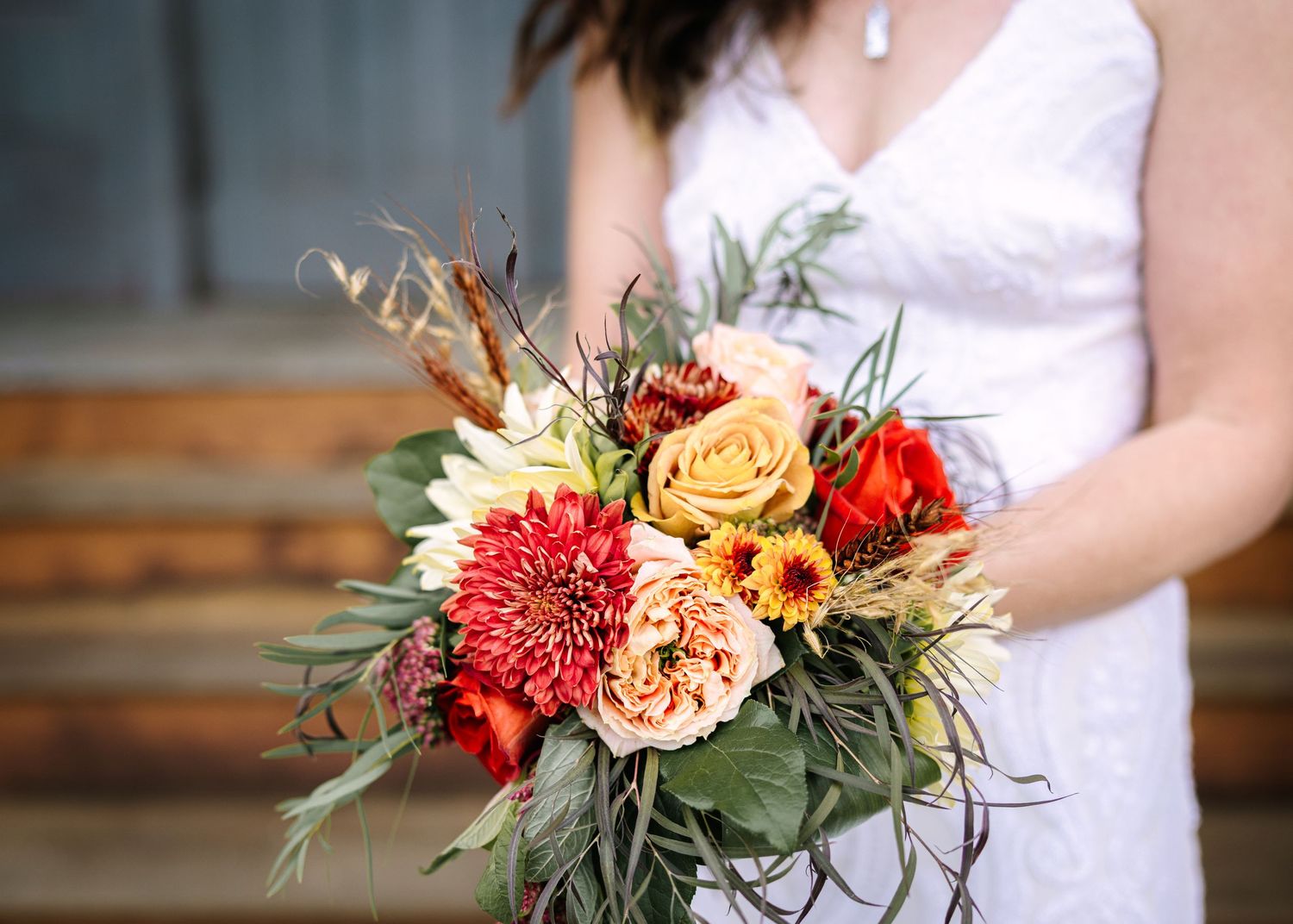 Wedding bouquet featuring vibrant red and peach flowers with green foliage accents in a rustic setting.