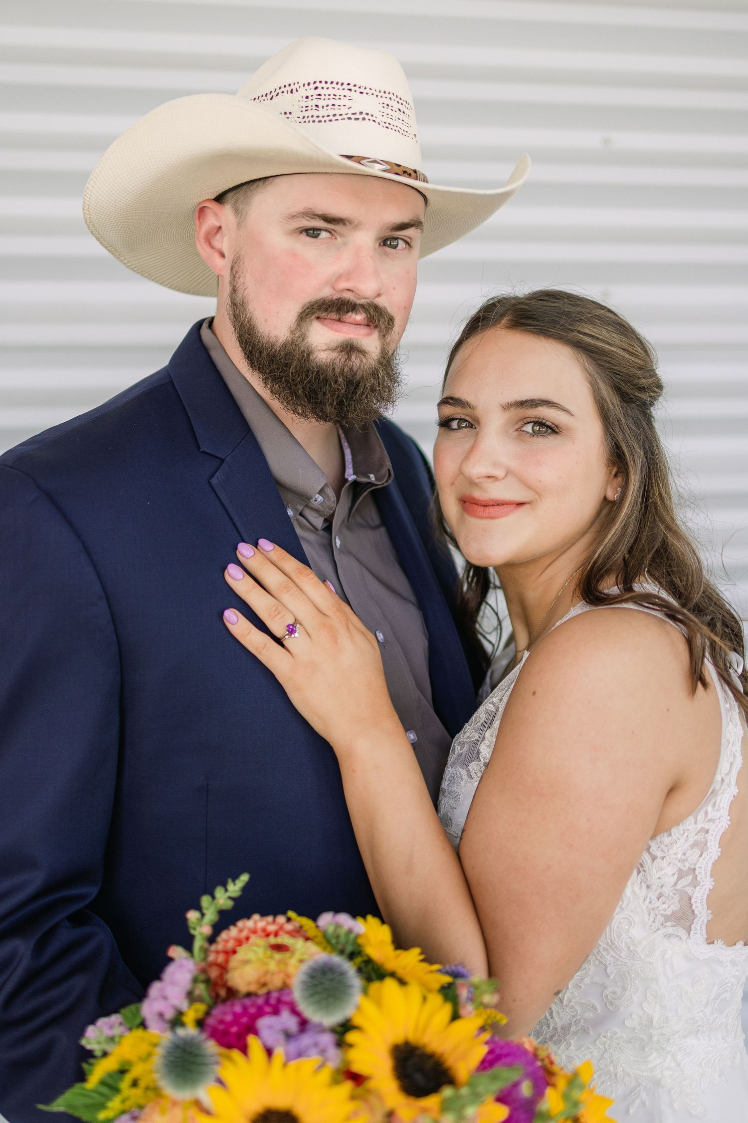 Newlyweds pose with vibrant sunflower bouquet against industrial backdrop. A photo by Helena wedding photographer Kelsea Laine Photography.