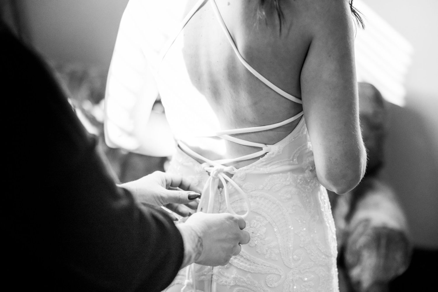 A bride in a white wedding dress gets help with the lacing and buttons on the back of her gown.