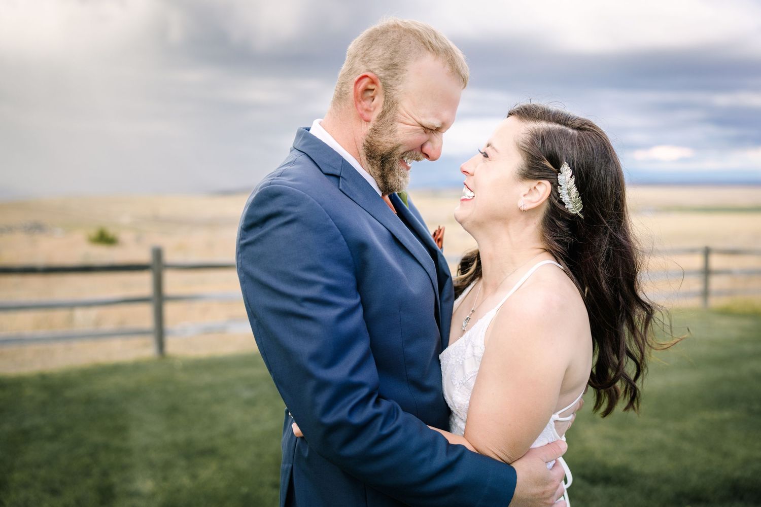 A couple in formal attire shares a romantic moment in a scenic outdoor field during golden hour.