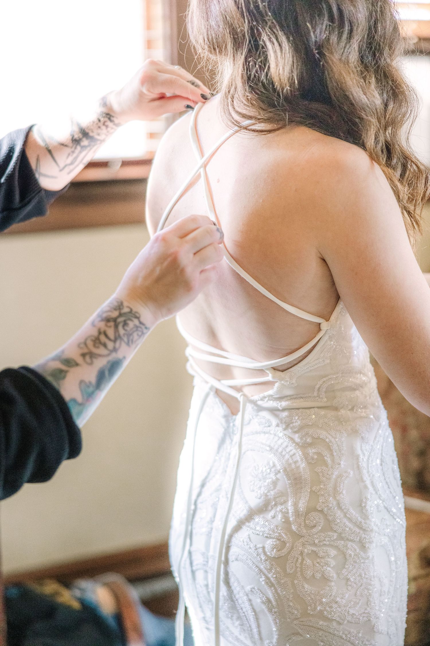 Close-up of a white lace wedding dress being laced up in the back. A bridal getting ready photo by Kelsea Laine Photography.
