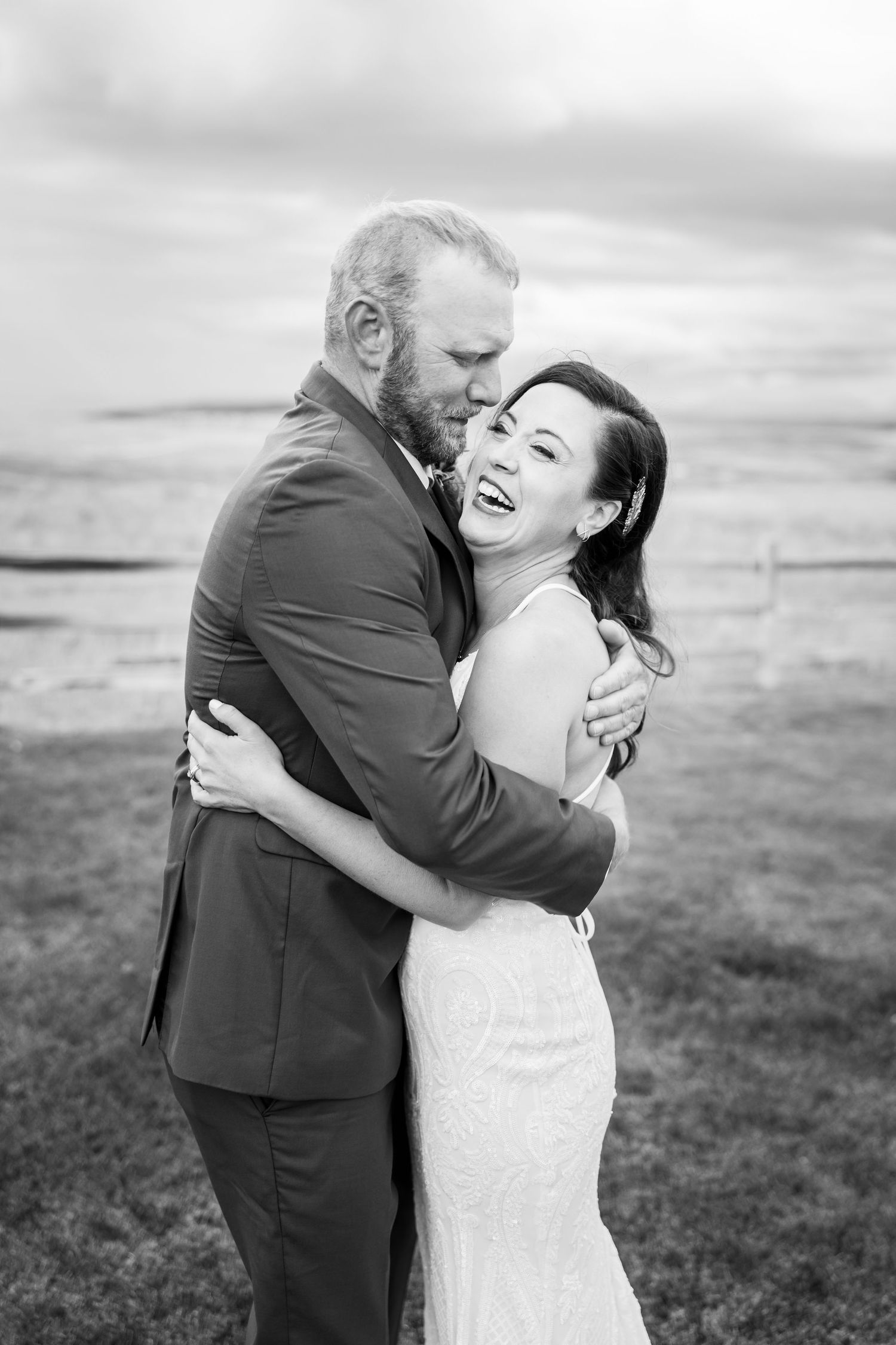 A romantic black and white photo series of a couple embracing and laughing together in an outdoor field setting.