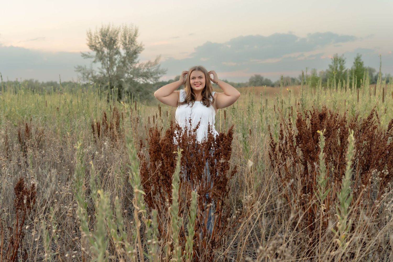 Portrait among tall grass with mountains in background at sunset.