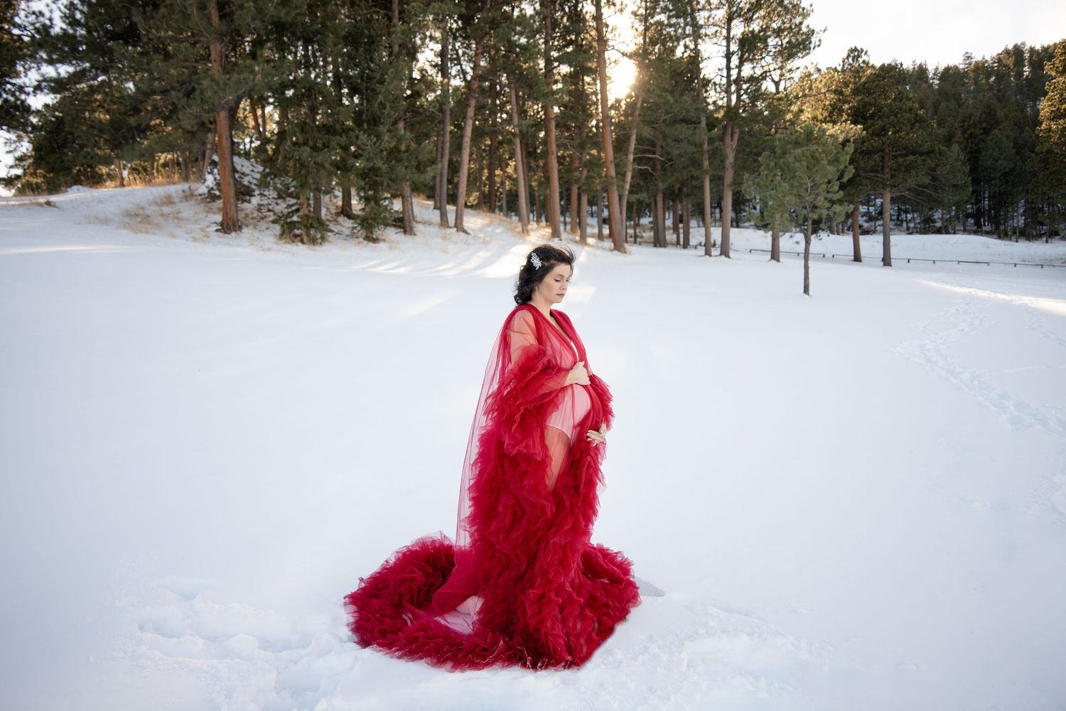 Dramatic red tulle gown flows in snow-covered winter forest at sunset.