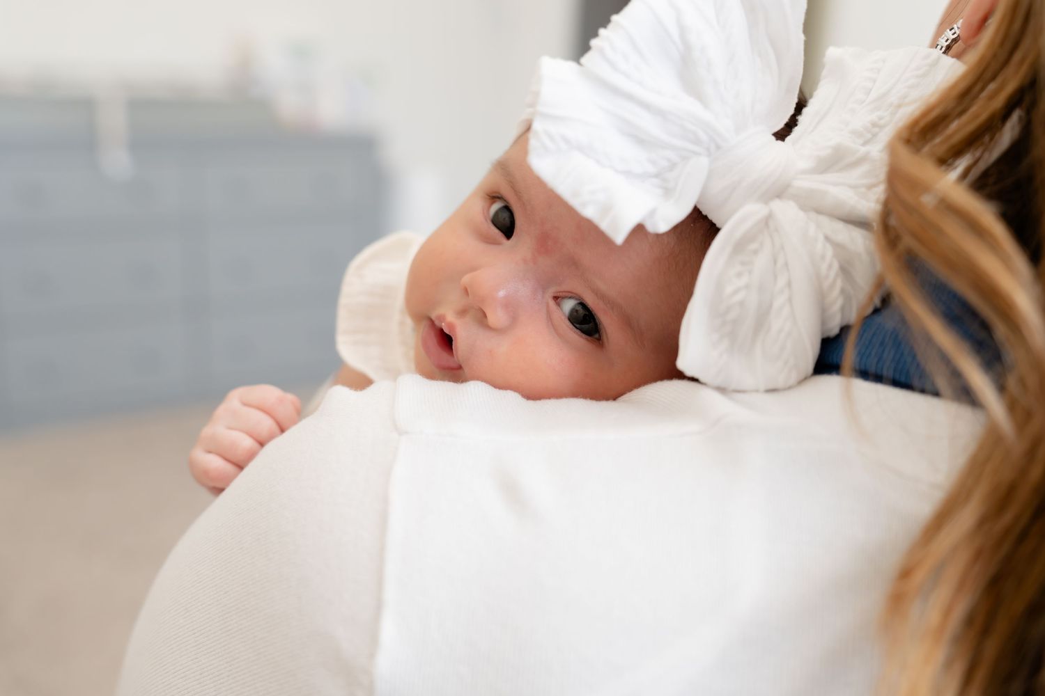 Sweet newborn baby in white outfit looking off to the side during photo session.