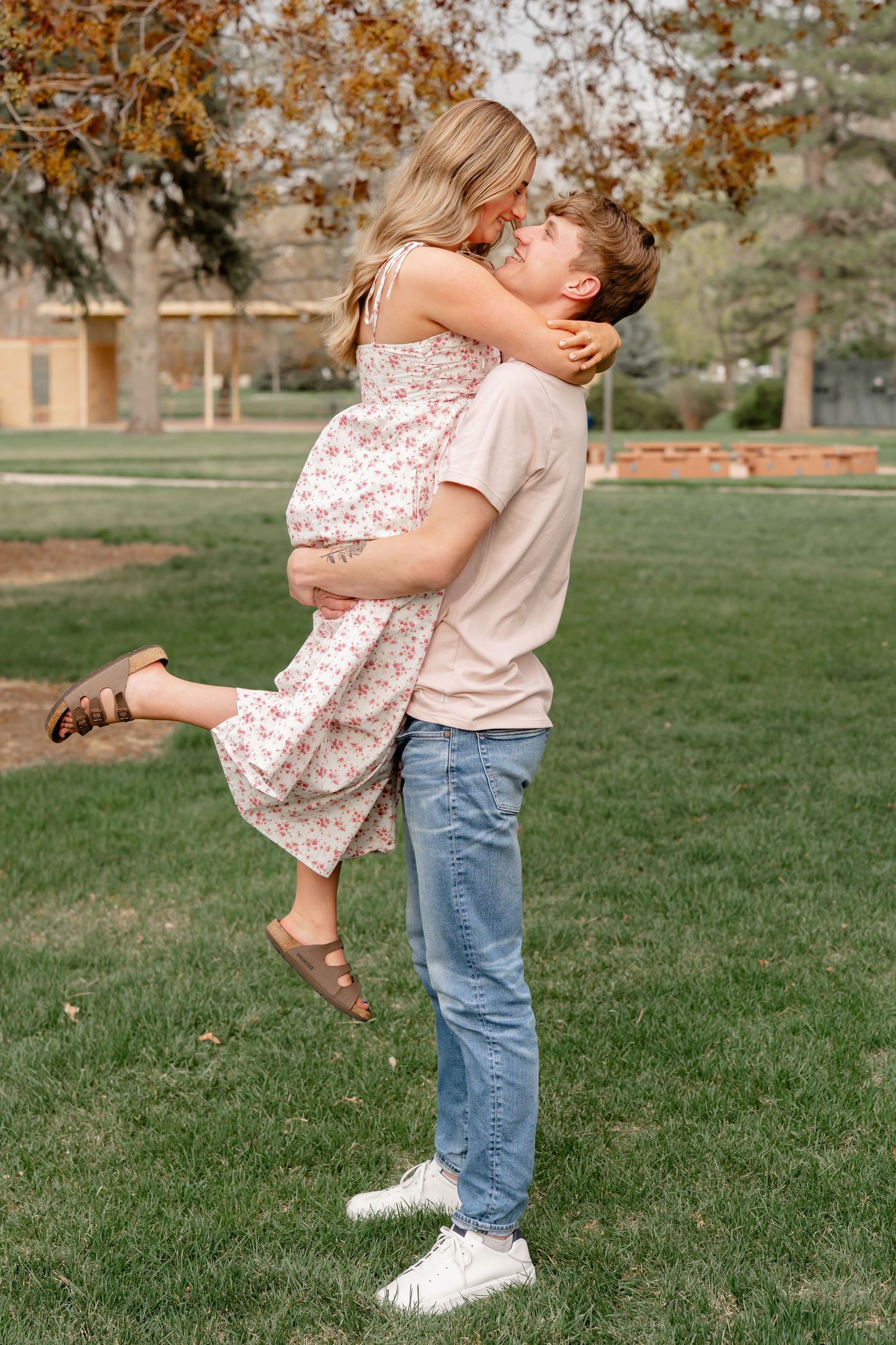 A couple sharing a playful moment in a park with autumn trees in the background.