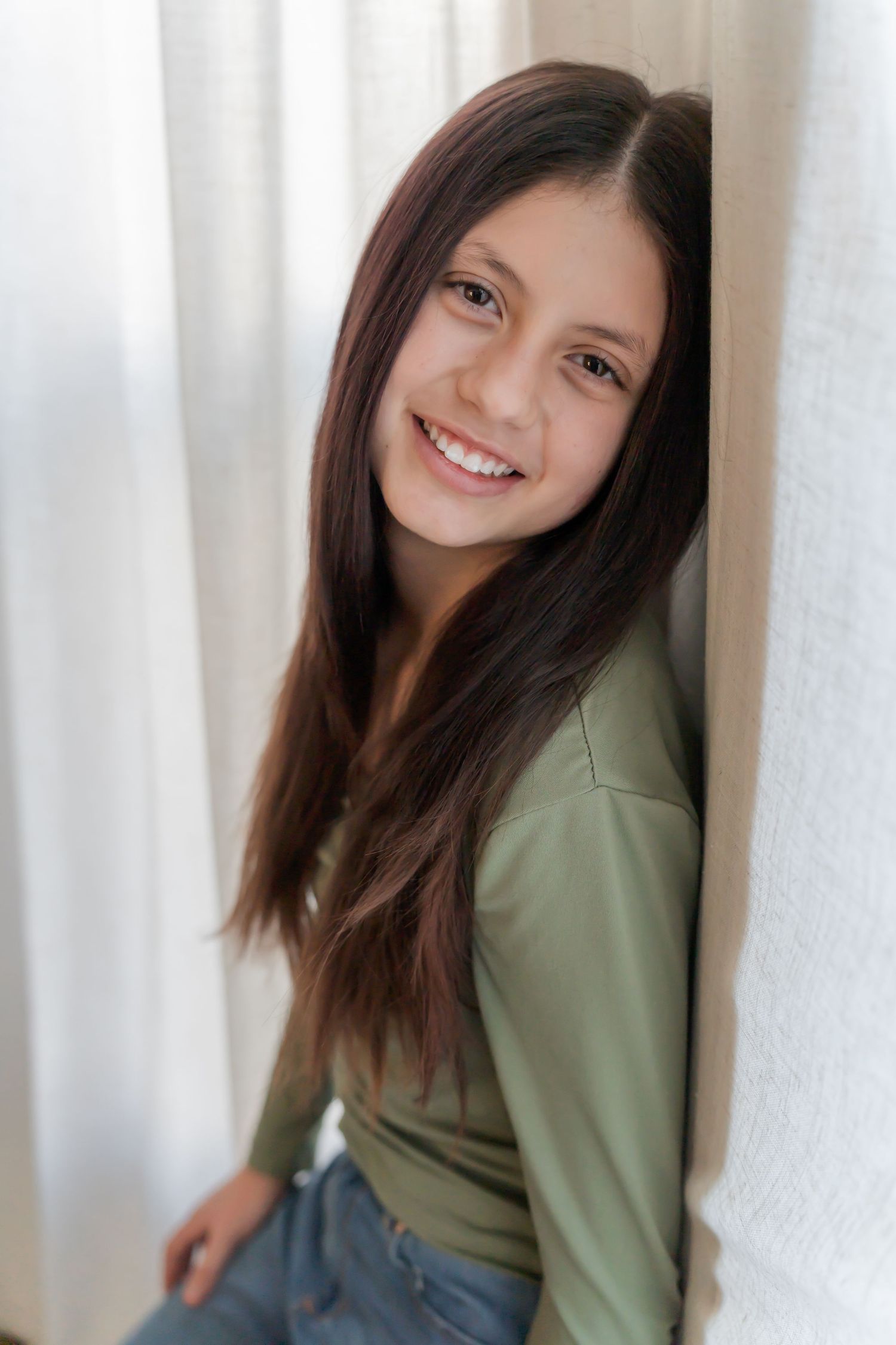 A person in a sage green sweater poses against a white wall in a series of casual portrait shots.