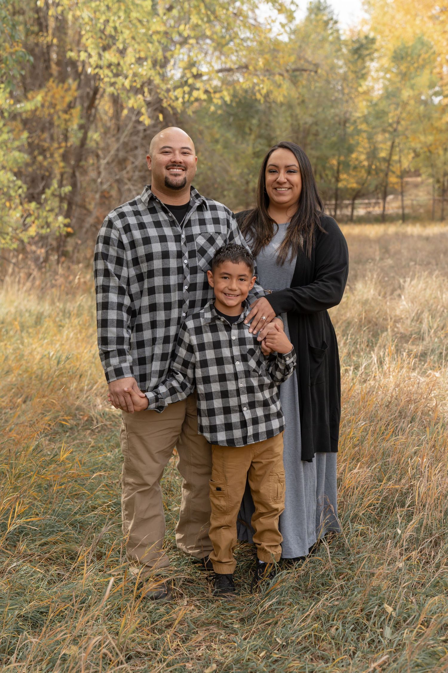 A family wearing matching plaid shirts poses together in a rustic outdoor setting.