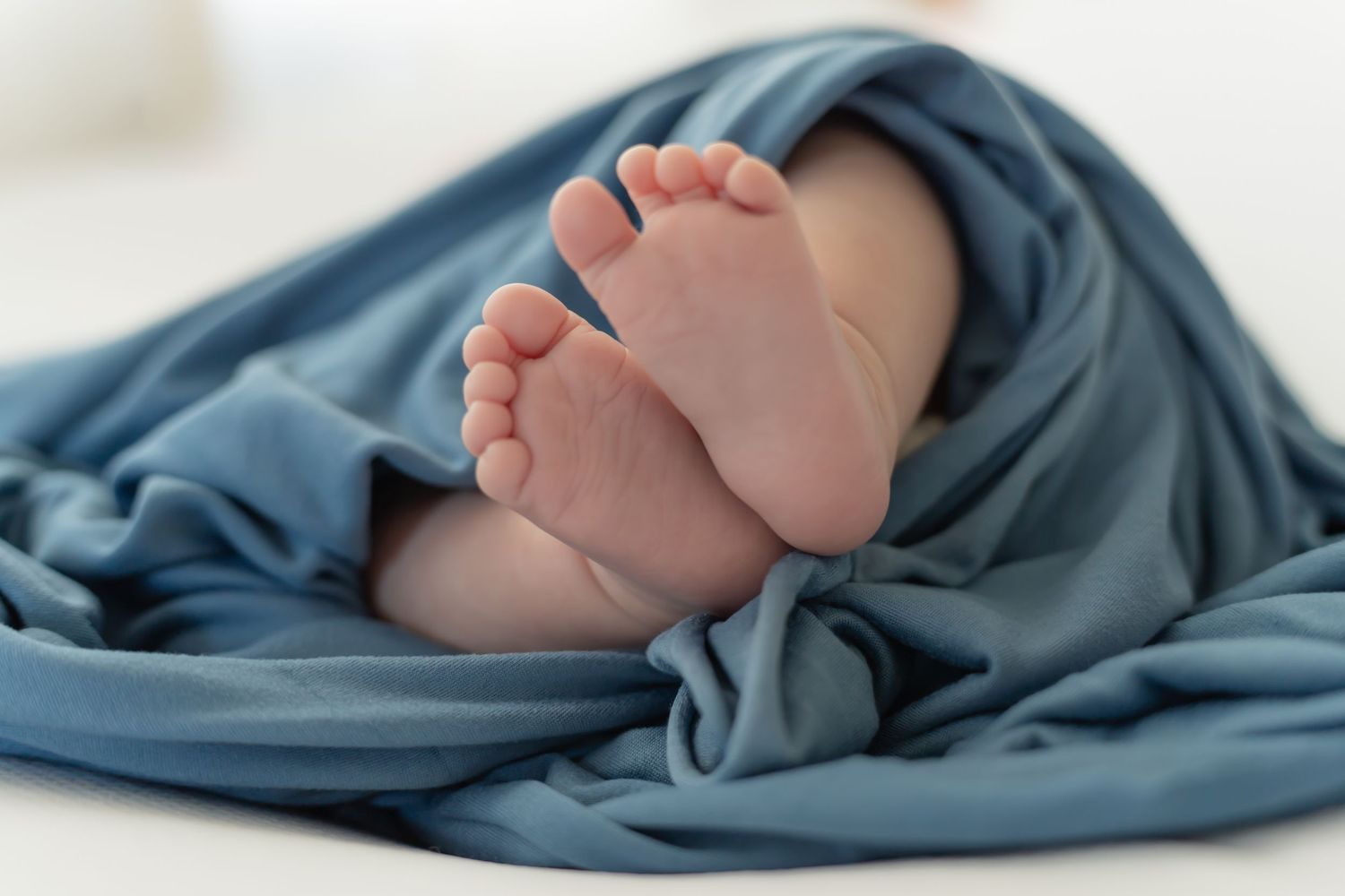 Small baby feet peek out from under a soft blue blanket in a tender newborn photography series.